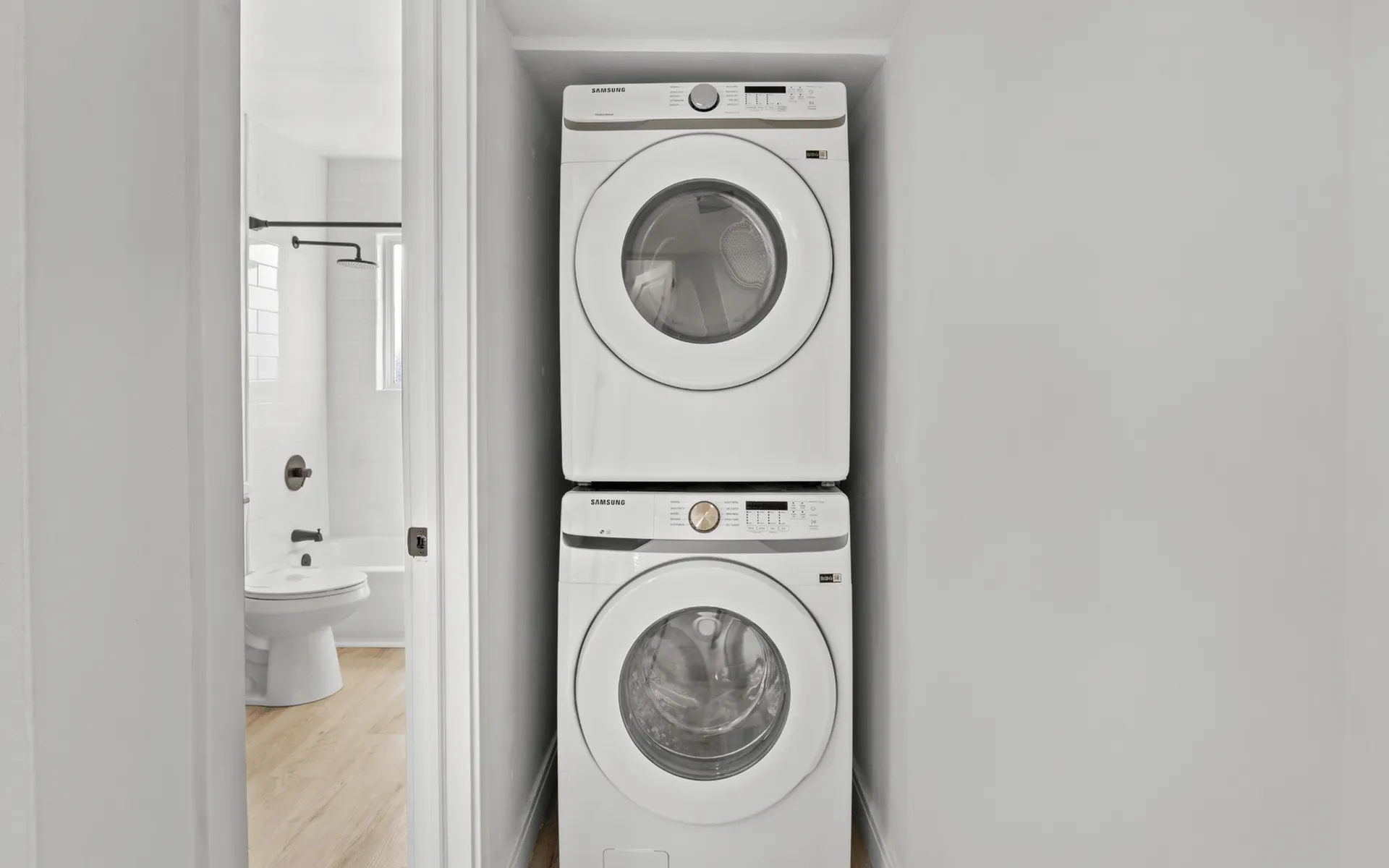 Compact laundry area featuring stackable washer and dryer next to a modern bathroom, optimizing apartment space efficiency.