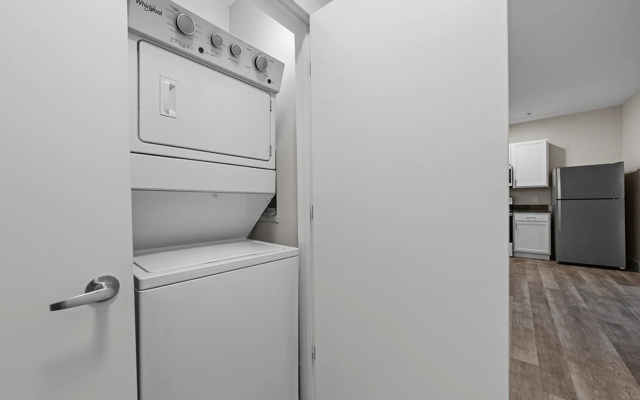 Modern apartment featuring an in-unit stacked washer and dryer adjacent to a sleek kitchen with stainless steel appliances and elegant wood flooring.
