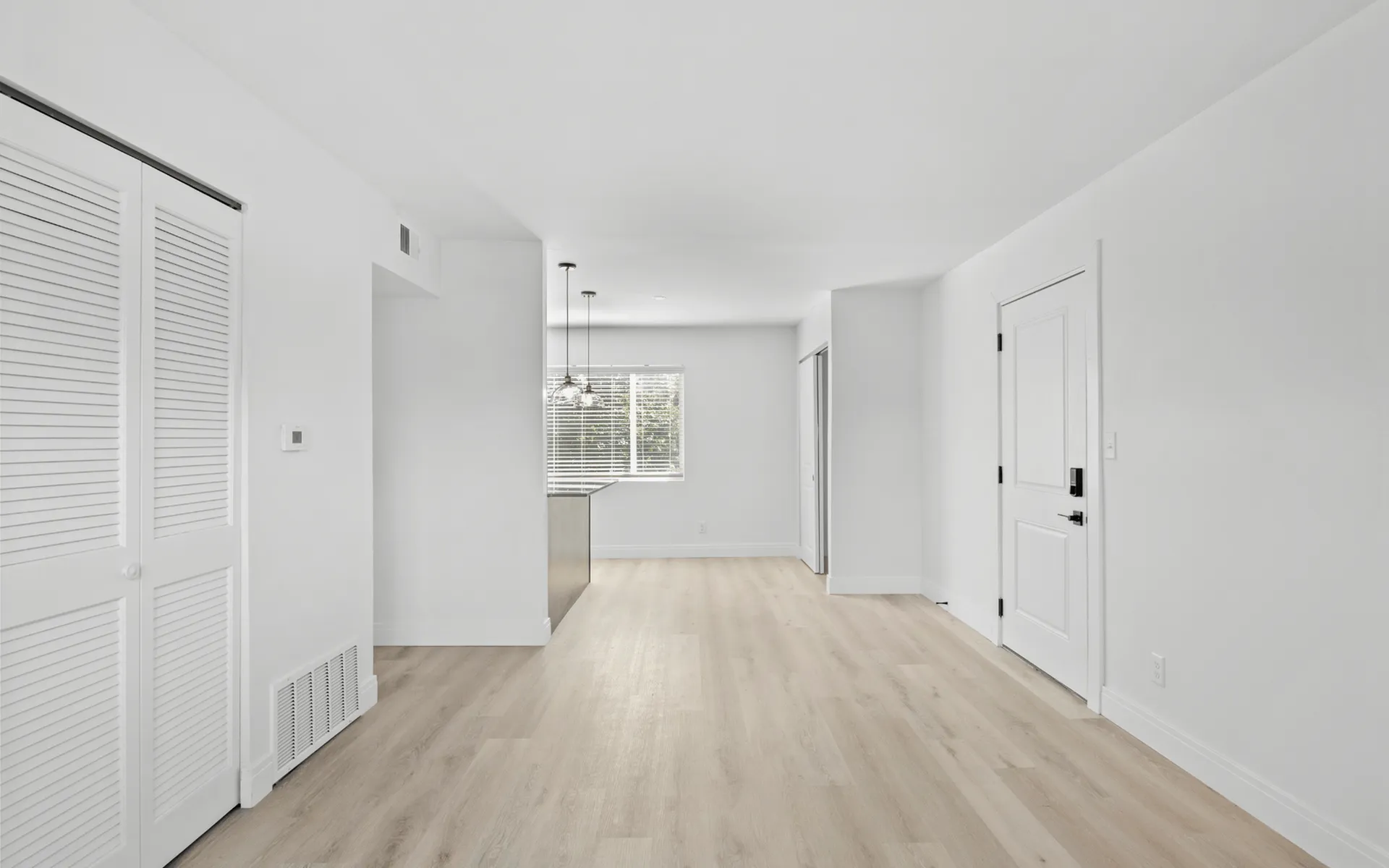 Bright open living space with sleek hardwood floors, modern pendant lighting, and large windows in a contemporary apartment.