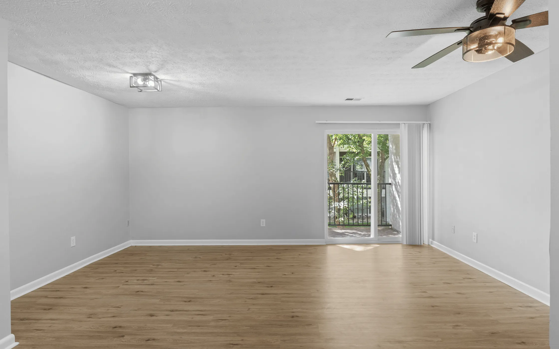 Bright and spacious living area with elegant wooden flooring, modern ceiling fan, and large sliding glass doors opening to a lush garden view.