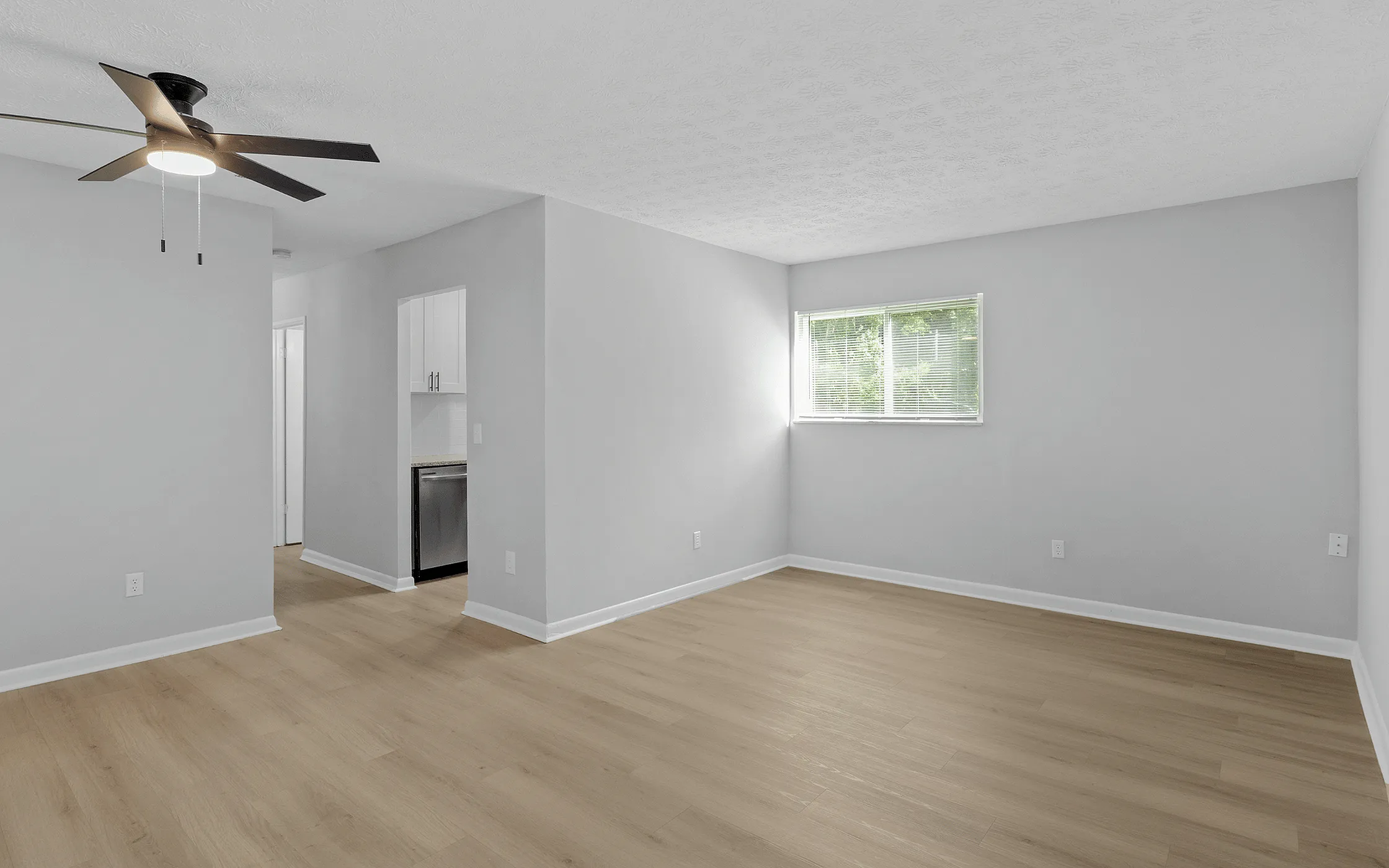 Bright and spacious living room with modern ceiling fan and elegant wooden flooring, featuring a large window that fills the area with natural light.