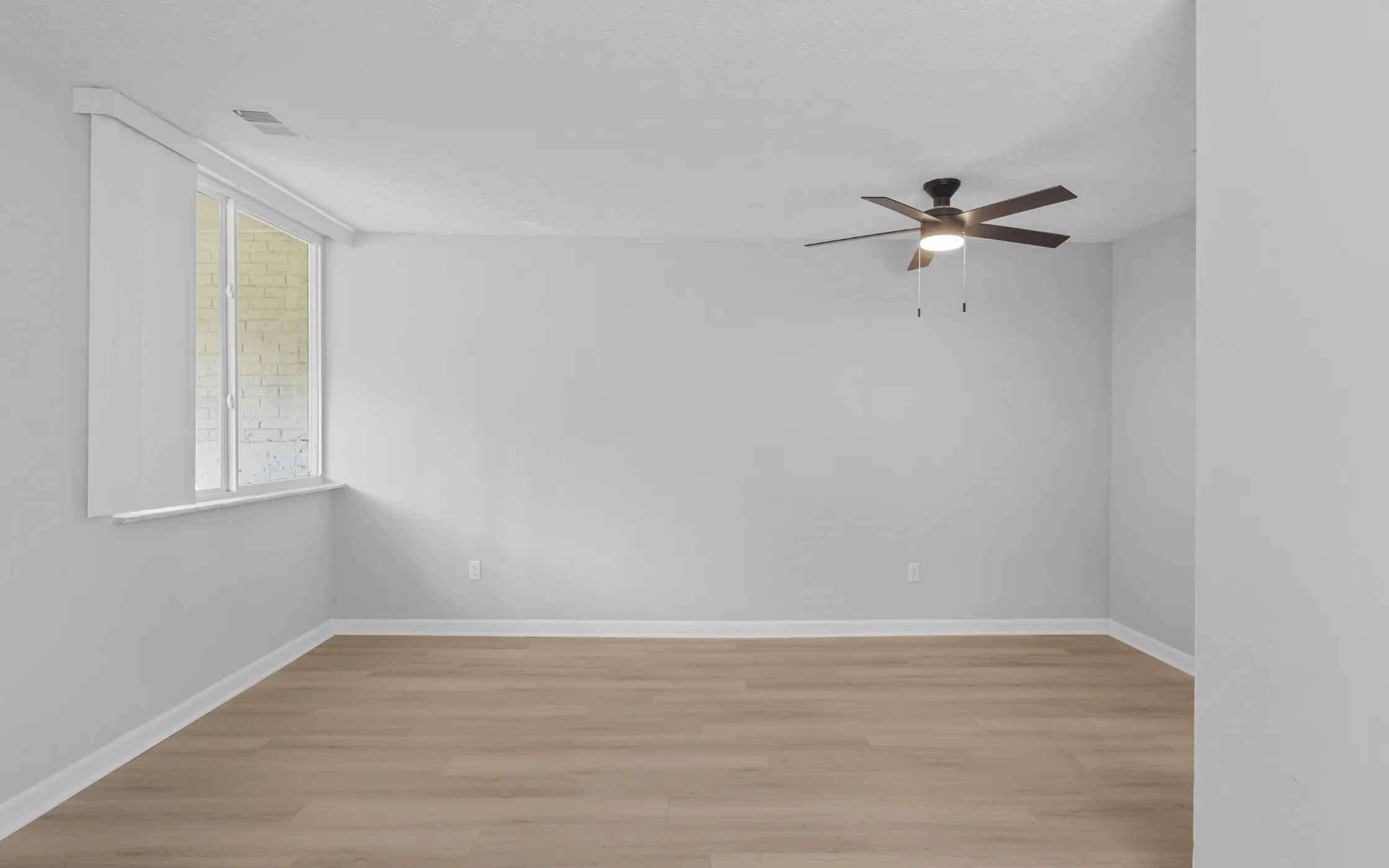 Bright, modern room with light wood flooring, fresh white walls, and a ceiling fan, ready for personal touches.