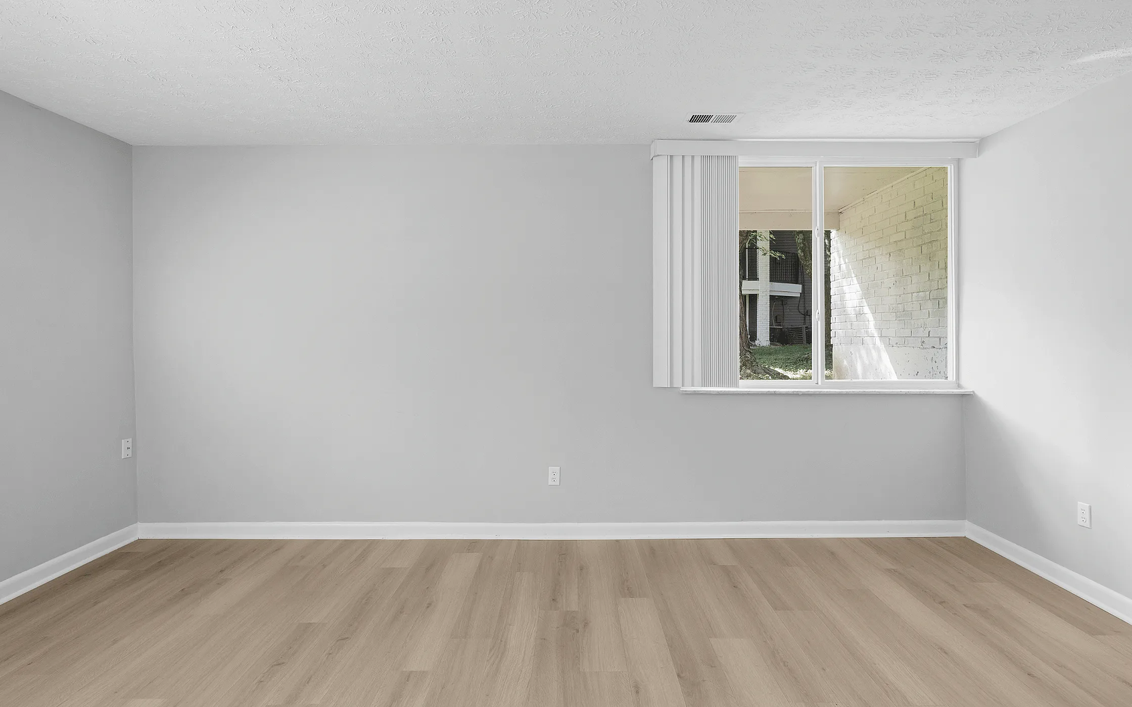 Bright, spacious room with sleek wooden flooring and a large window offering a serene view, perfect for customization.