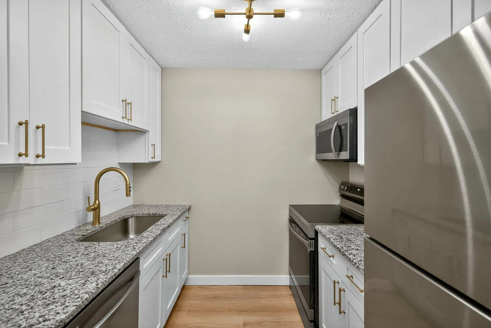 Elegant kitchen with granite countertops, white cabinetry, stainless steel appliances, and modern lighting.