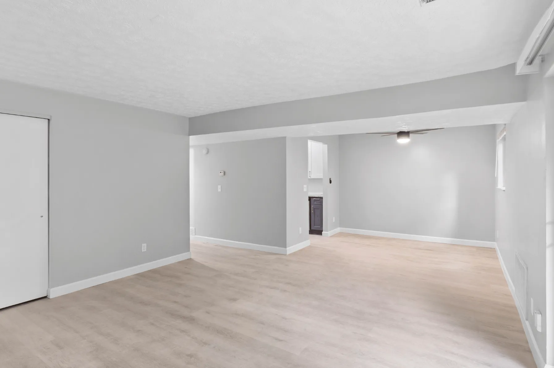 Spacious open floor plan with light wood flooring, modern gray walls, and a cozy ceiling fan in a bright living area.