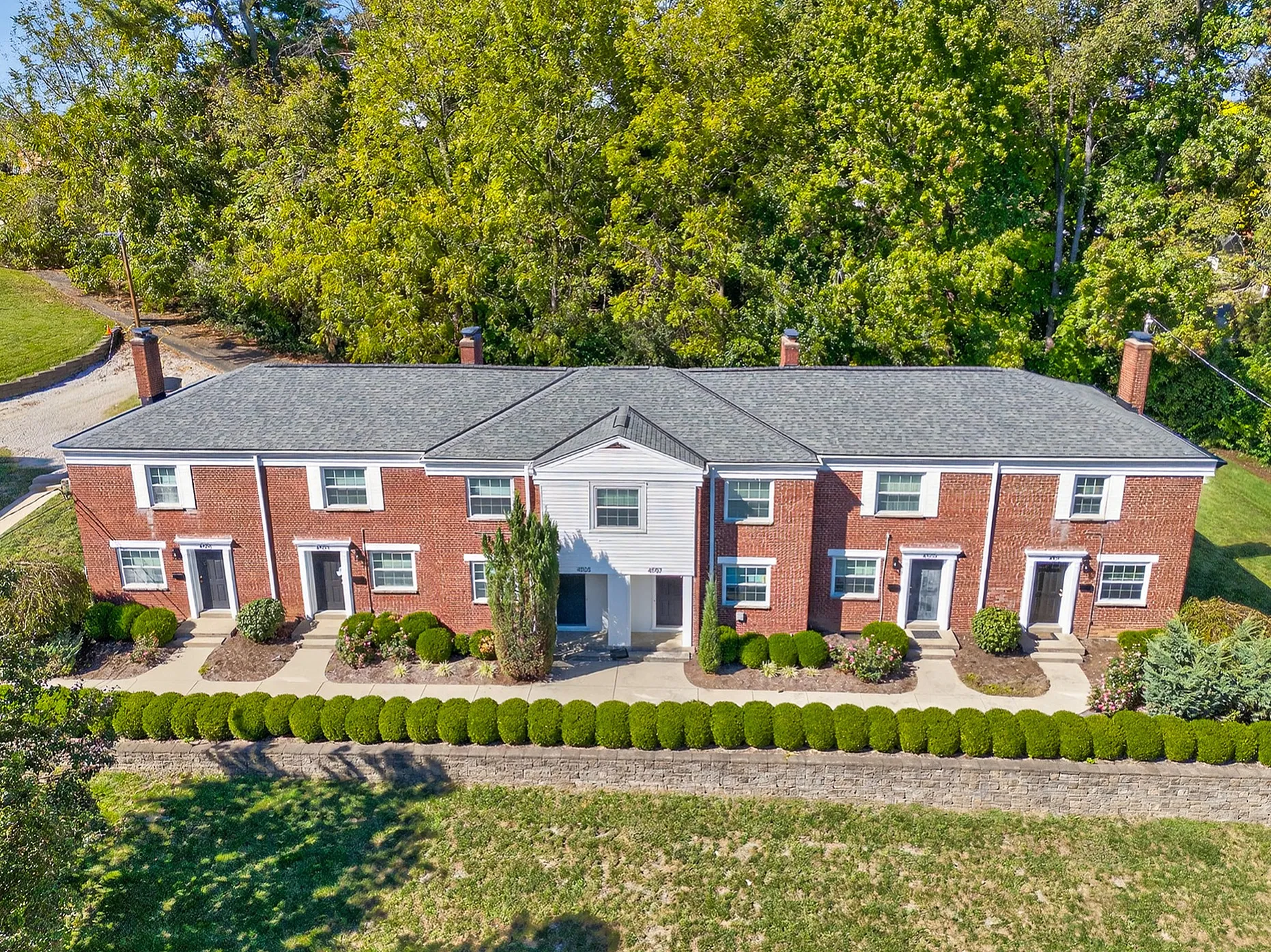 Charming brick apartment complex nestled among lush greenery, featuring classic architecture and well-maintained landscaping for a serene living environment.