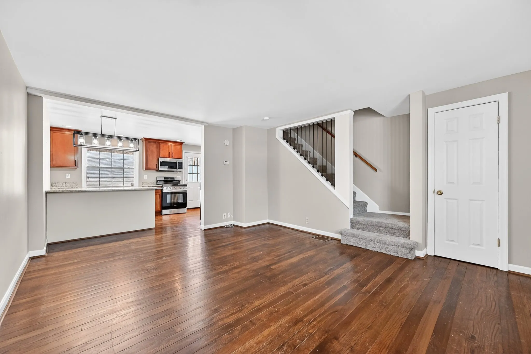 Inviting open-concept living area with sleek hardwood floors, modern kitchen with stainless steel appliances, and elegant staircase.