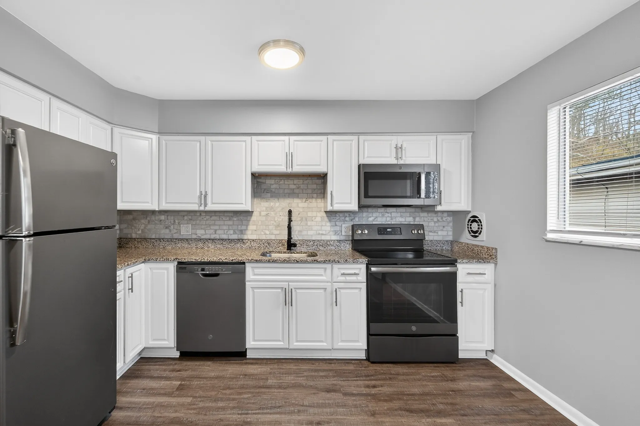 Contemporary kitchen with stainless steel appliances, sleek granite countertops, and elegant white cabinetry, featuring a cozy window view.