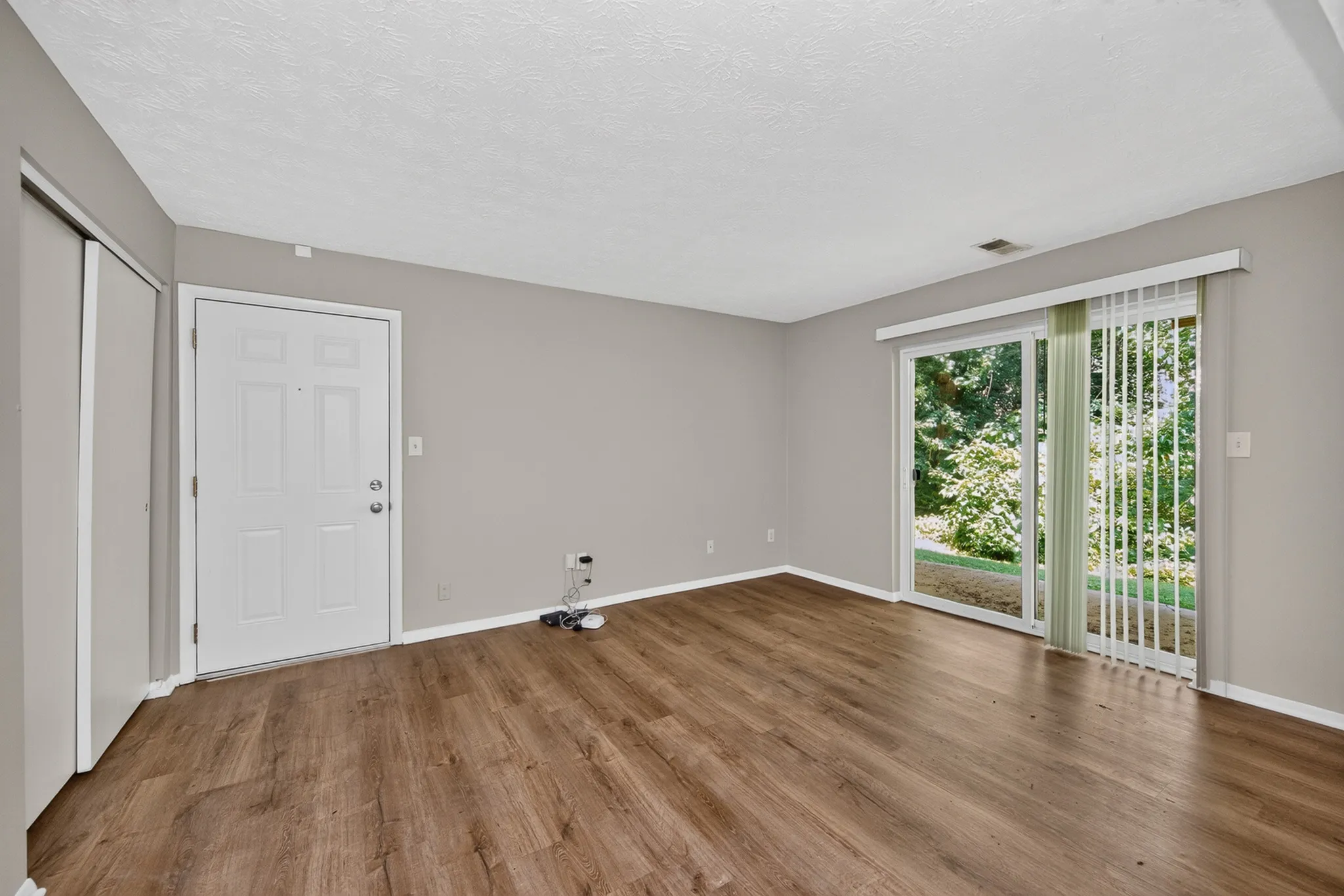 Spacious living room with elegant laminate flooring and large sliding glass doors opening to a lush garden view.