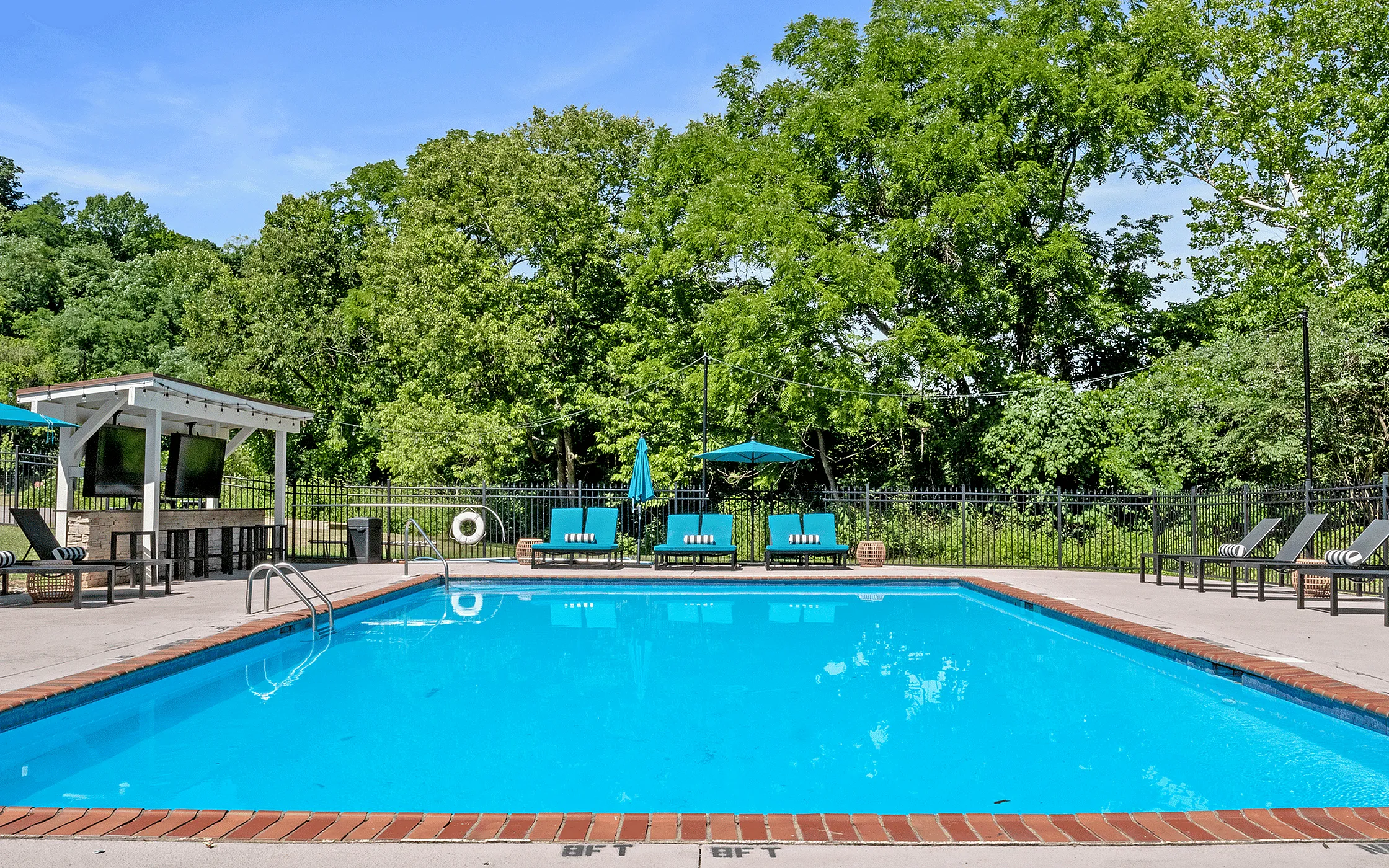 Inviting outdoor pool area with vibrant blue loungers and umbrellas surrounded by lush greenery, perfect for relaxation and leisure.