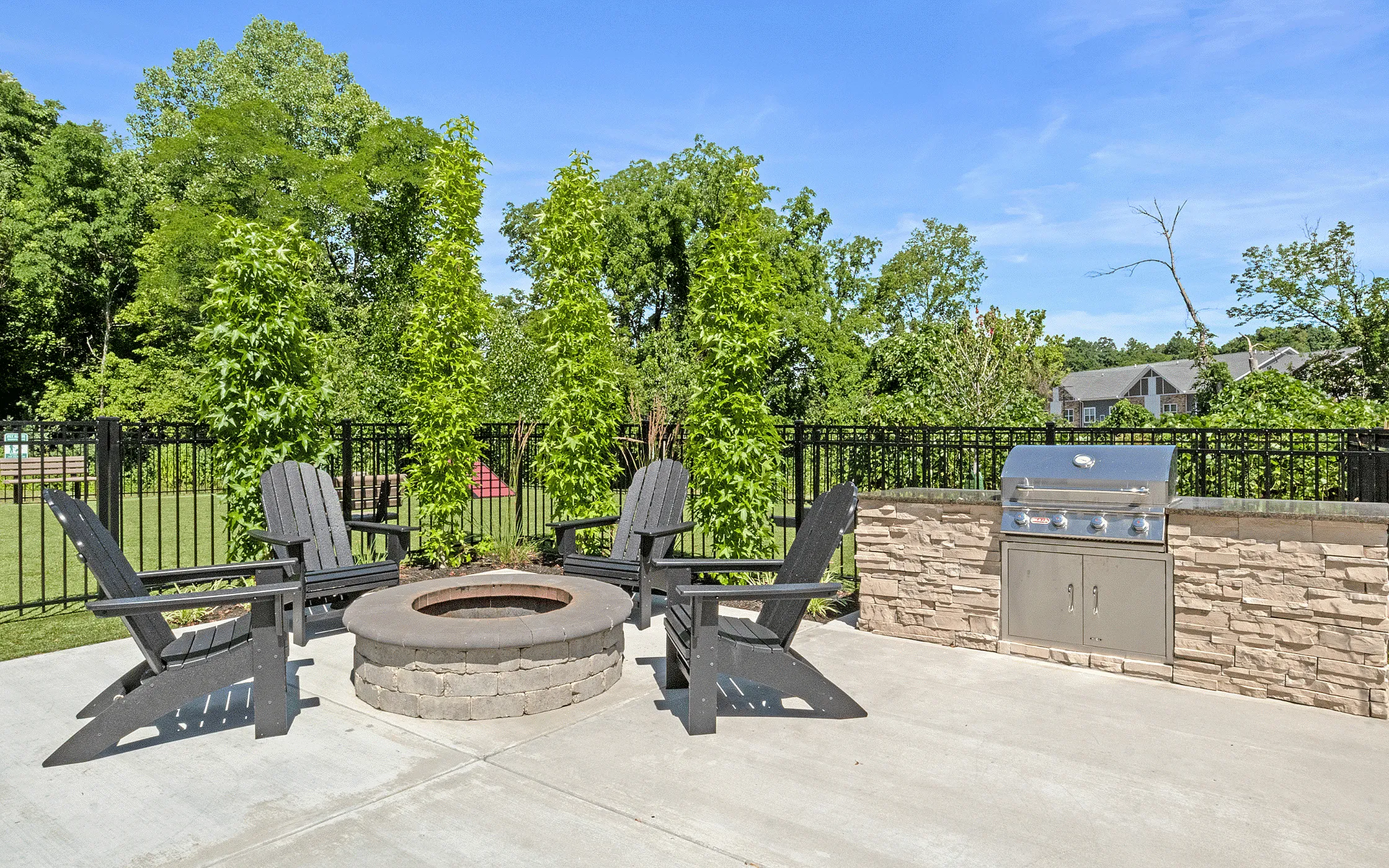 Inviting outdoor patio featuring a cozy fire pit surrounded by stylish Adirondack chairs and a modern grill station, perfect for entertaining amidst lush greenery.