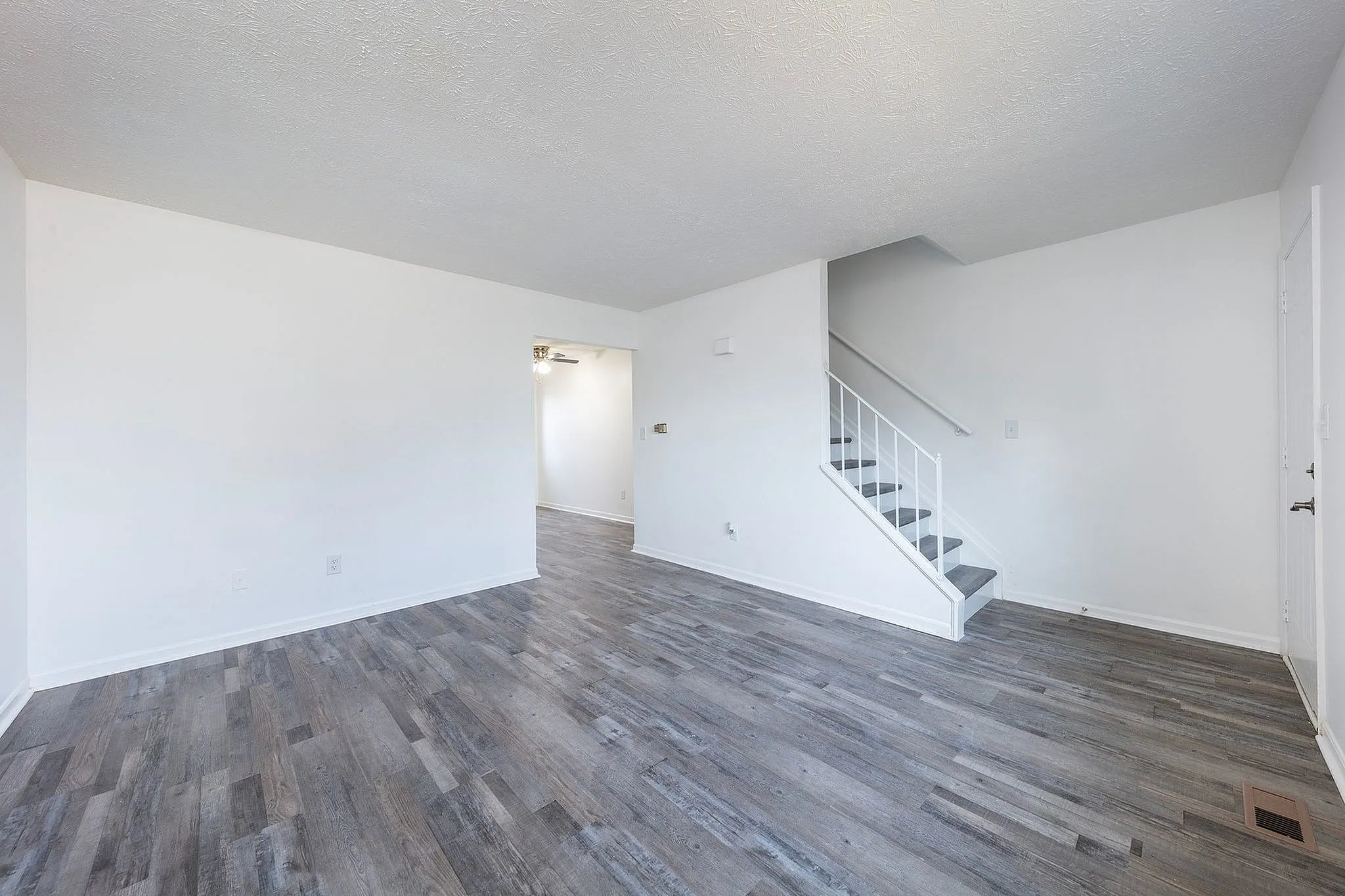 Fairfield Square Apartments with vinyl wood flooring throughout, Modern living space with elegant grey flooring and bright white walls, featuring a stylish staircase leading to upper level.