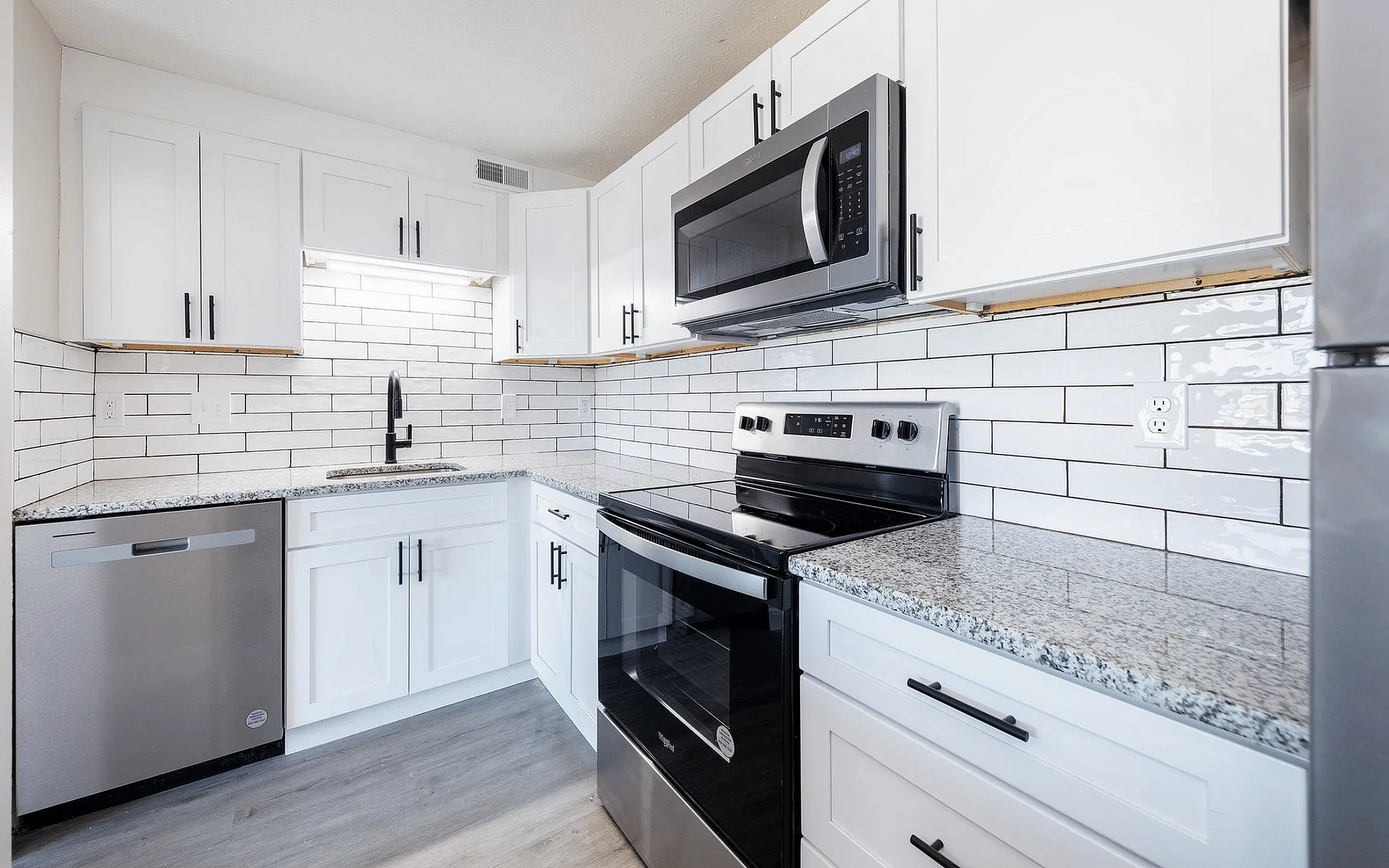 Fairfield Square Apartments Stainless Steel Appliances,Modern kitchen with sleek white cabinetry, granite countertops, stainless steel appliances, and a stylish subway tile backsplash.