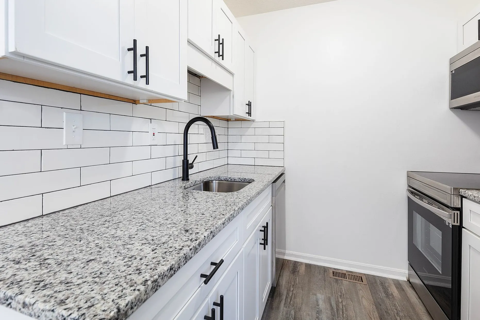 Fairfield Square Apartments Renovated Kitchen with Granite Countertops, Modern kitchen with sleek granite countertops, stainless steel appliances, and stylish white cabinetry with elegant black fixtures.