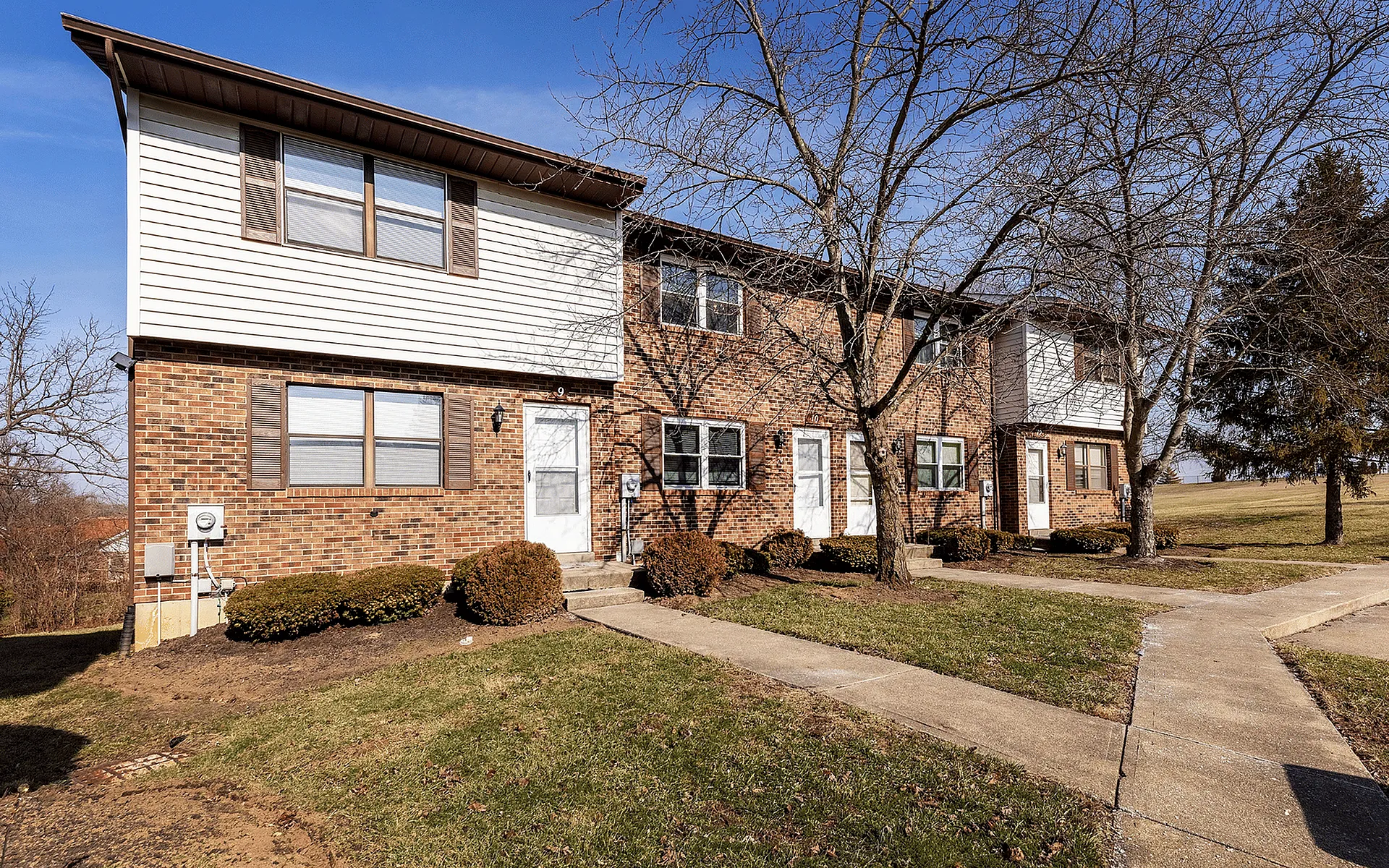 Charming two-story brick townhouses with manicured lawns and tree-lined pathways, perfect for a peaceful suburban lifestyle.