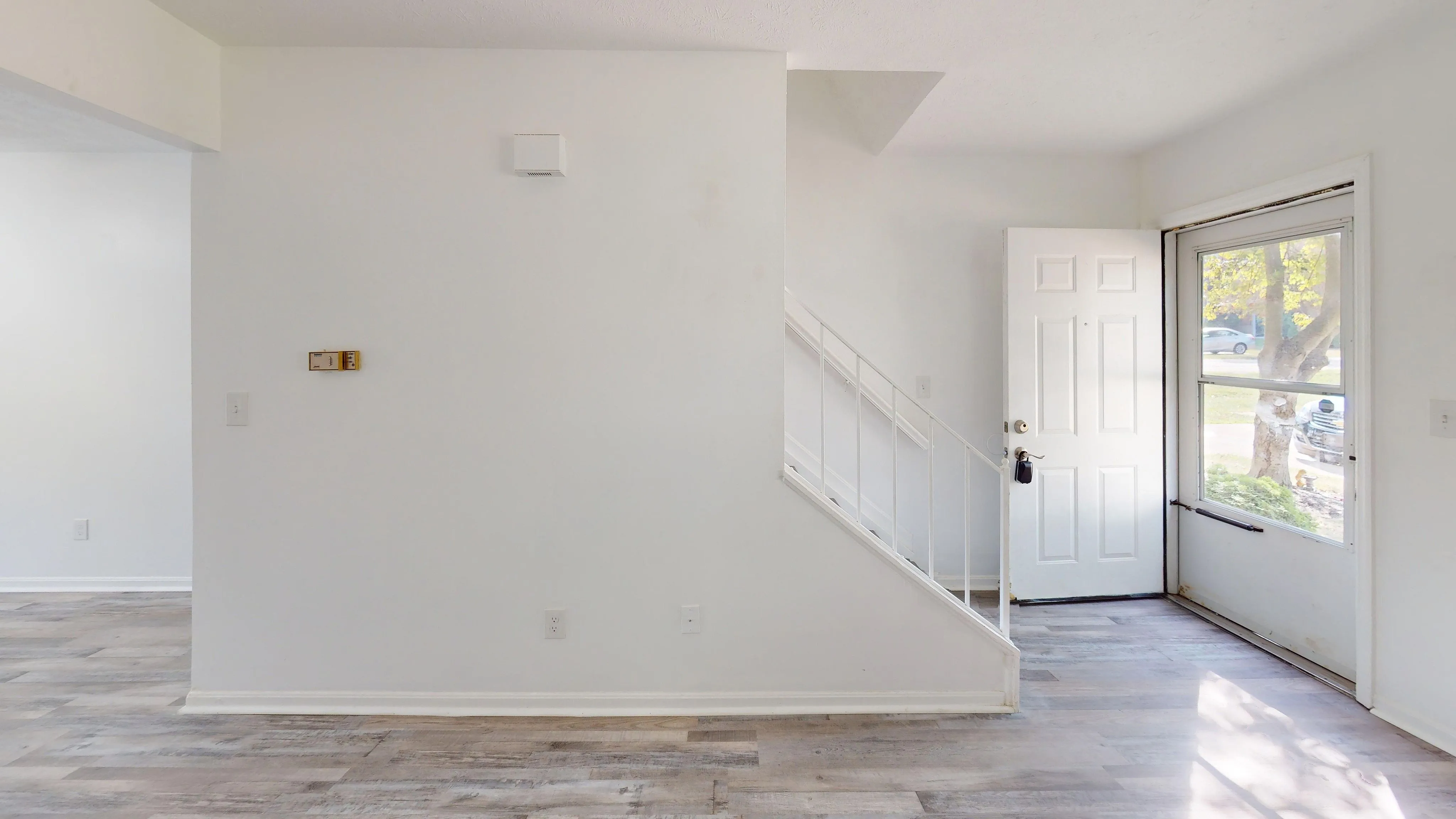 Bright entryway with sleek laminate flooring, open staircase, and a large window for natural light.
