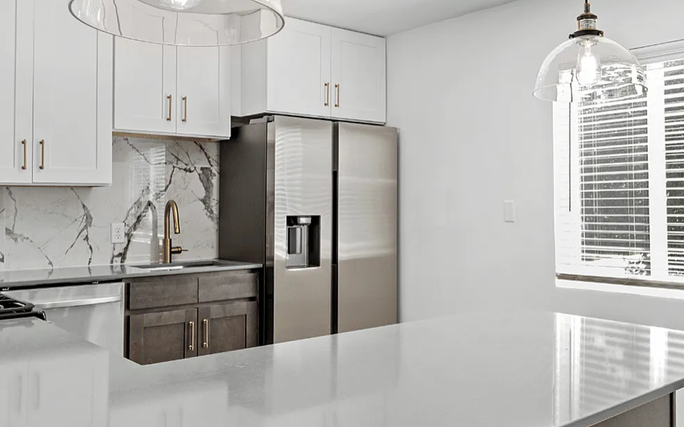 Modern kitchen with glossy countertops, elegant pendant lighting, stainless steel appliances, and large windows for natural light.