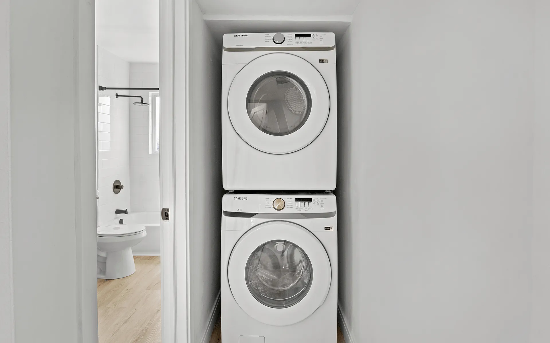 Modern apartment laundry space with stackable washer and dryer next to a pristine bathroom, showcasing efficient use of space.