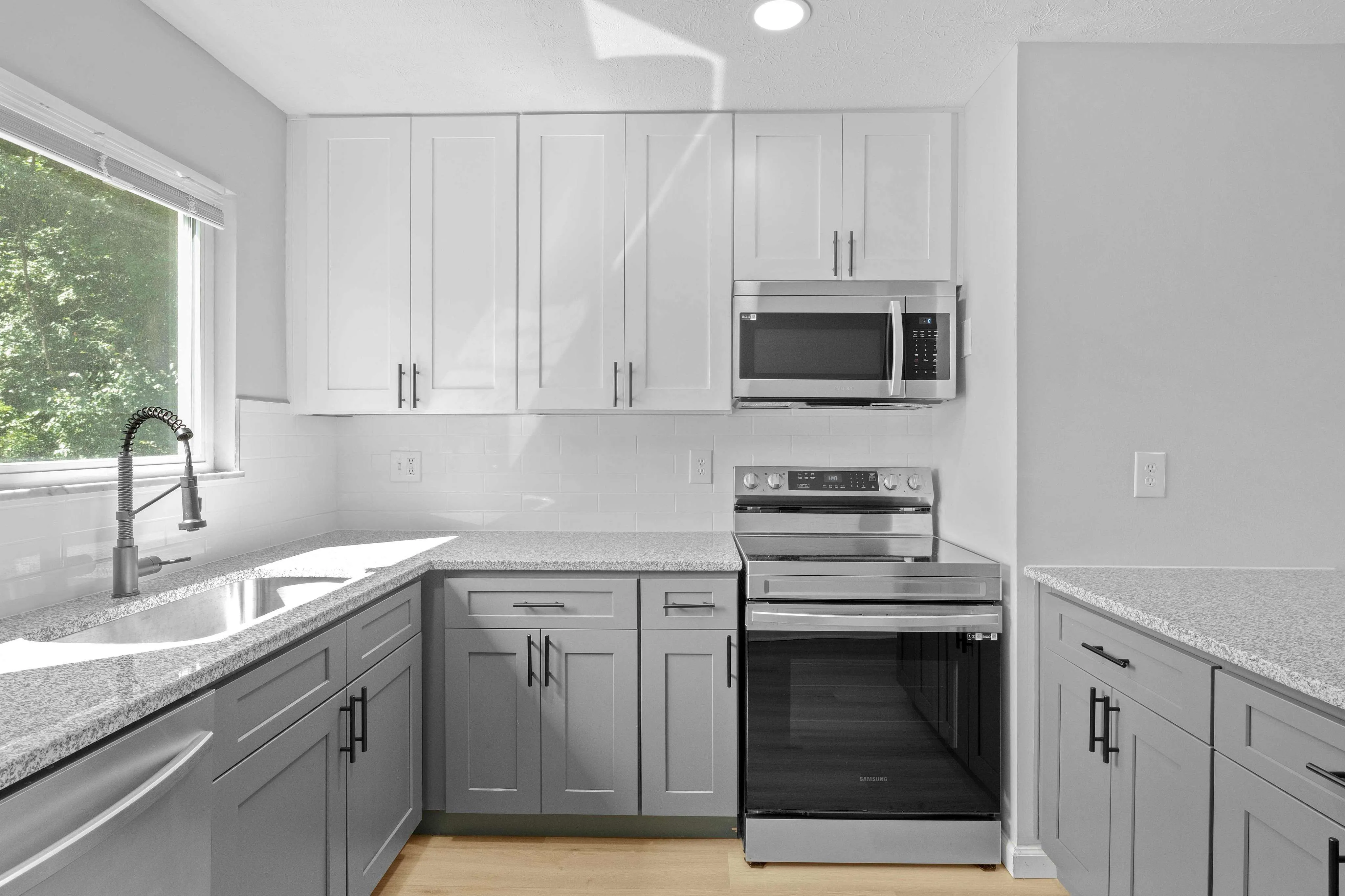 Modern kitchen with sleek white cabinets, stainless steel appliances, and elegant granite countertops, featuring ample natural light through a large window.