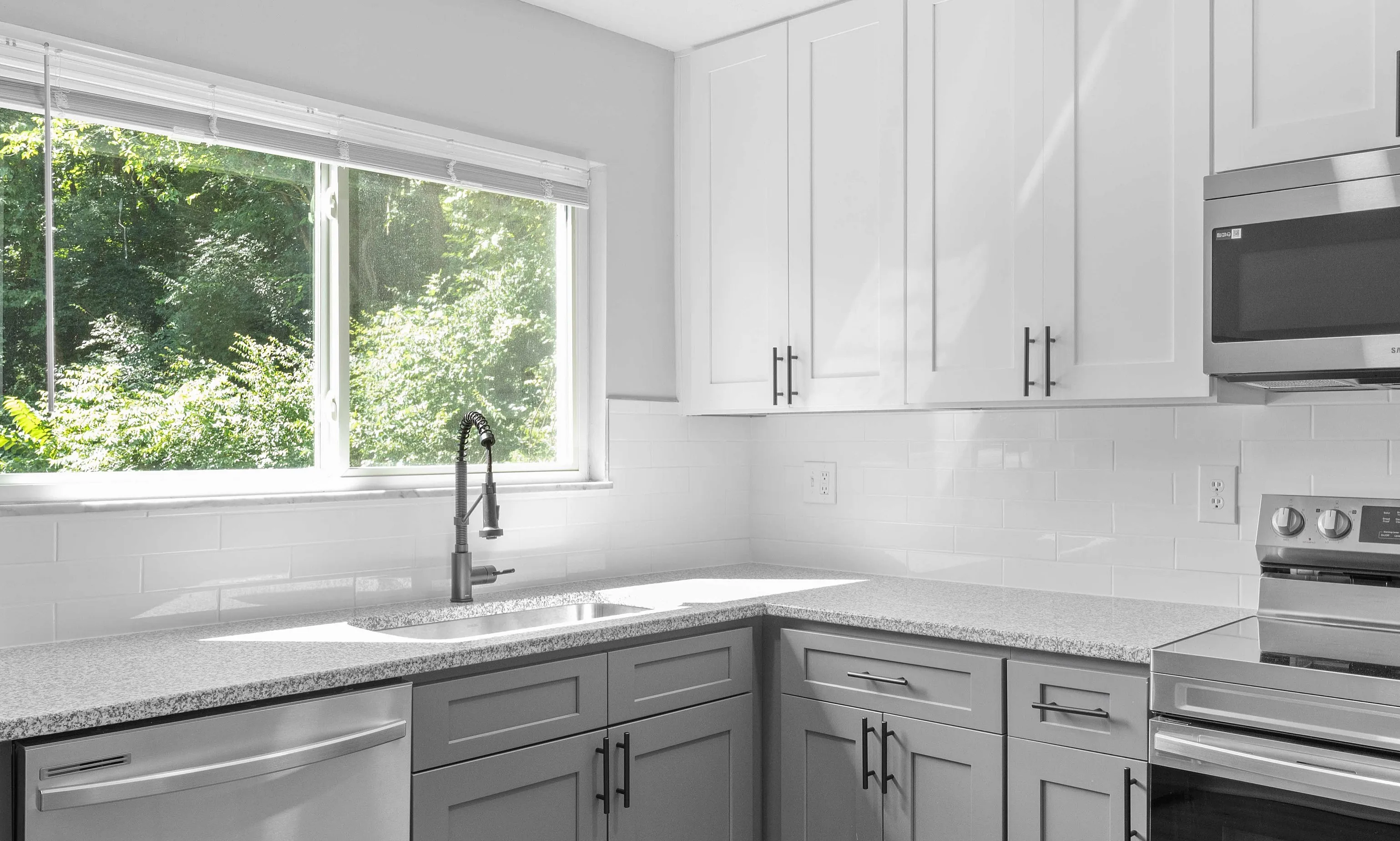 Modern kitchen with sleek gray cabinets, stainless steel appliances, and a sunlit window offering lush green views.
