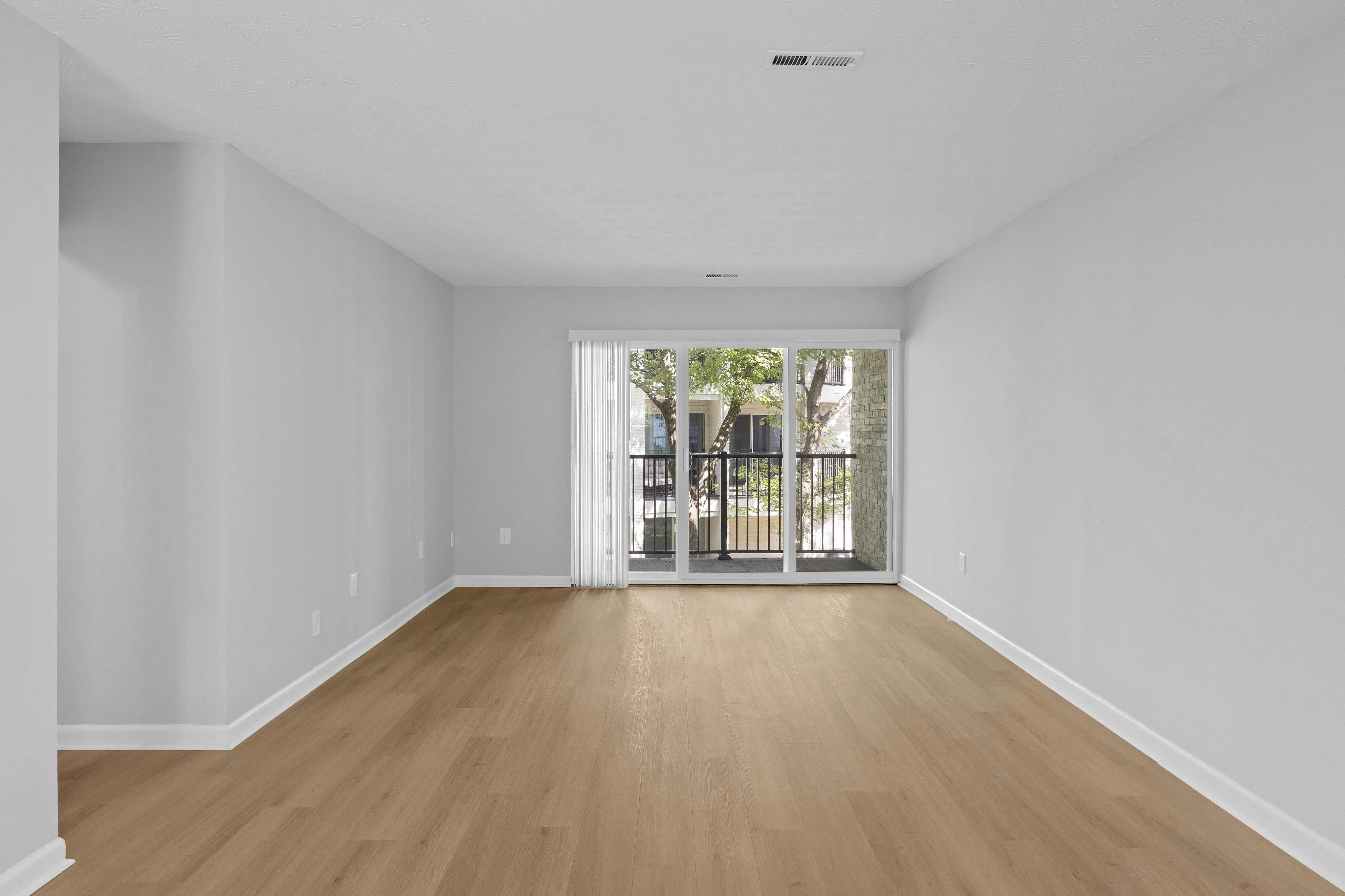 Bright and spacious living area with elegant hardwood floors and large windows opening to a serene balcony view.
