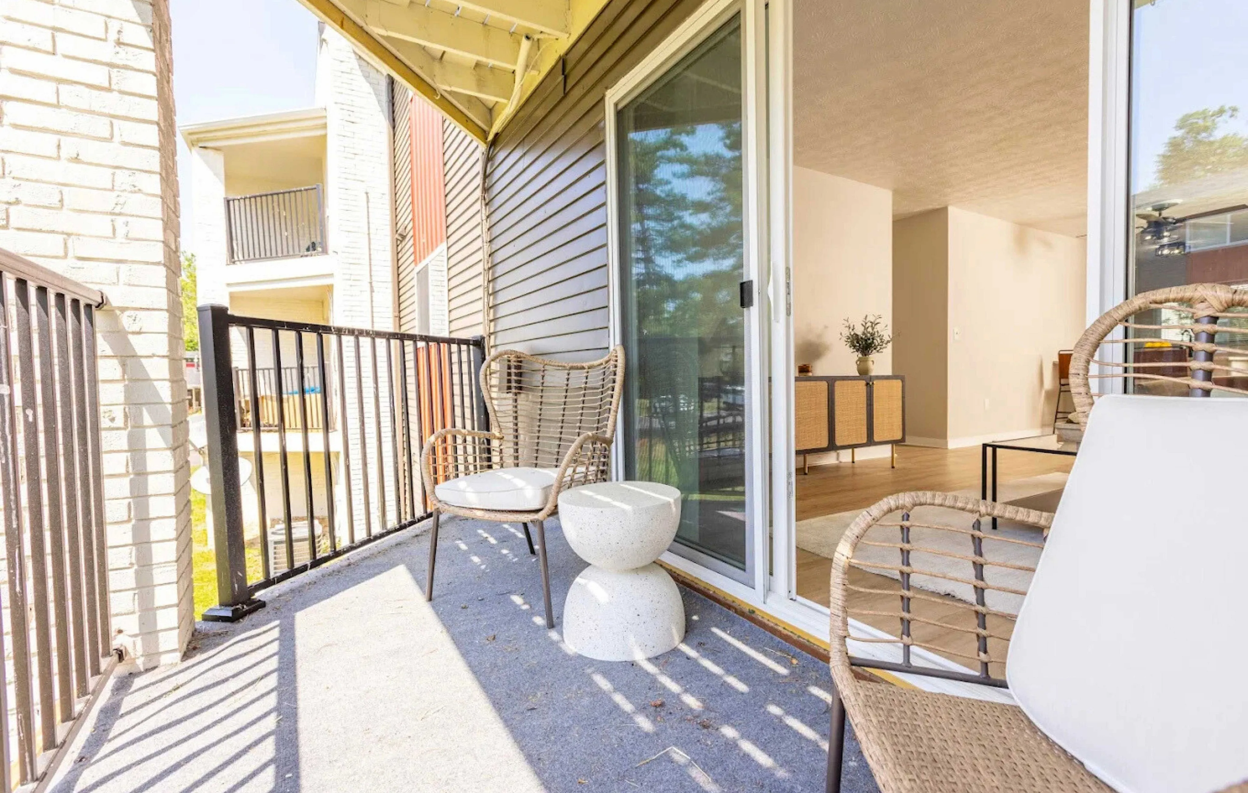 Alcove apartments in cincinnati, Charming apartment balcony with wicker chairs overlooking a serene outdoor view, leading into a bright, modern living space.
