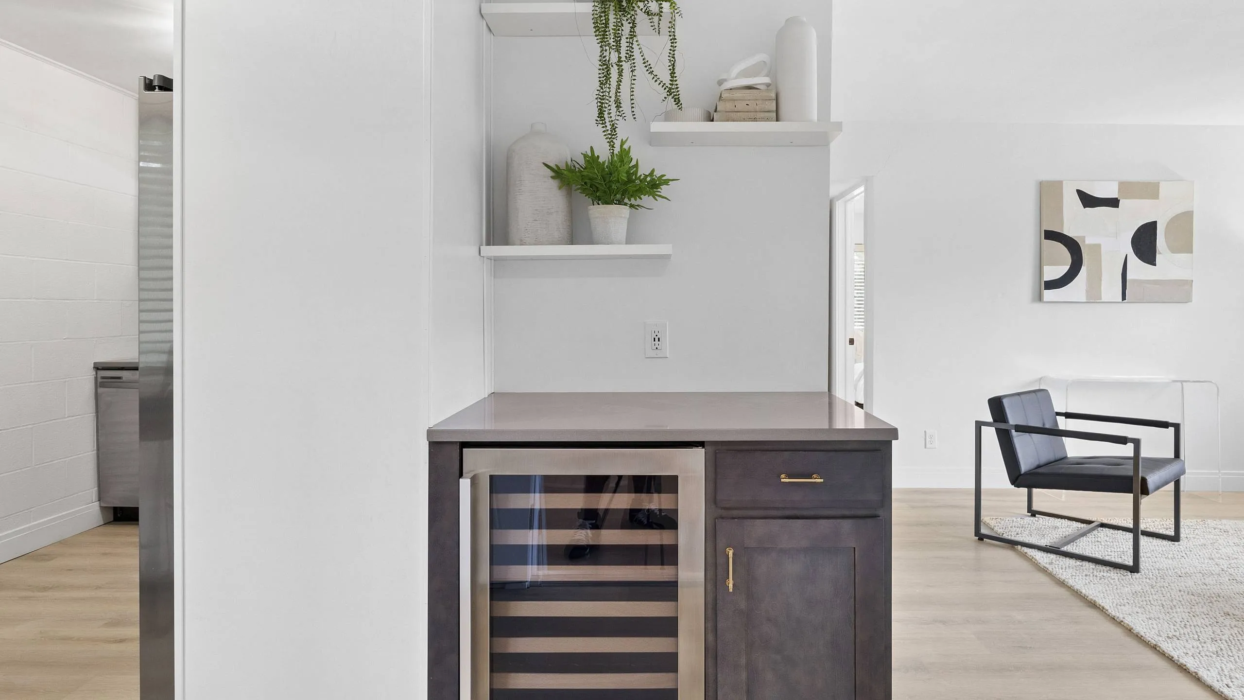 Chic modern living space with a sleek wine fridge, decorative shelving, and stylish furniture accentuating a contemporary aesthetic.