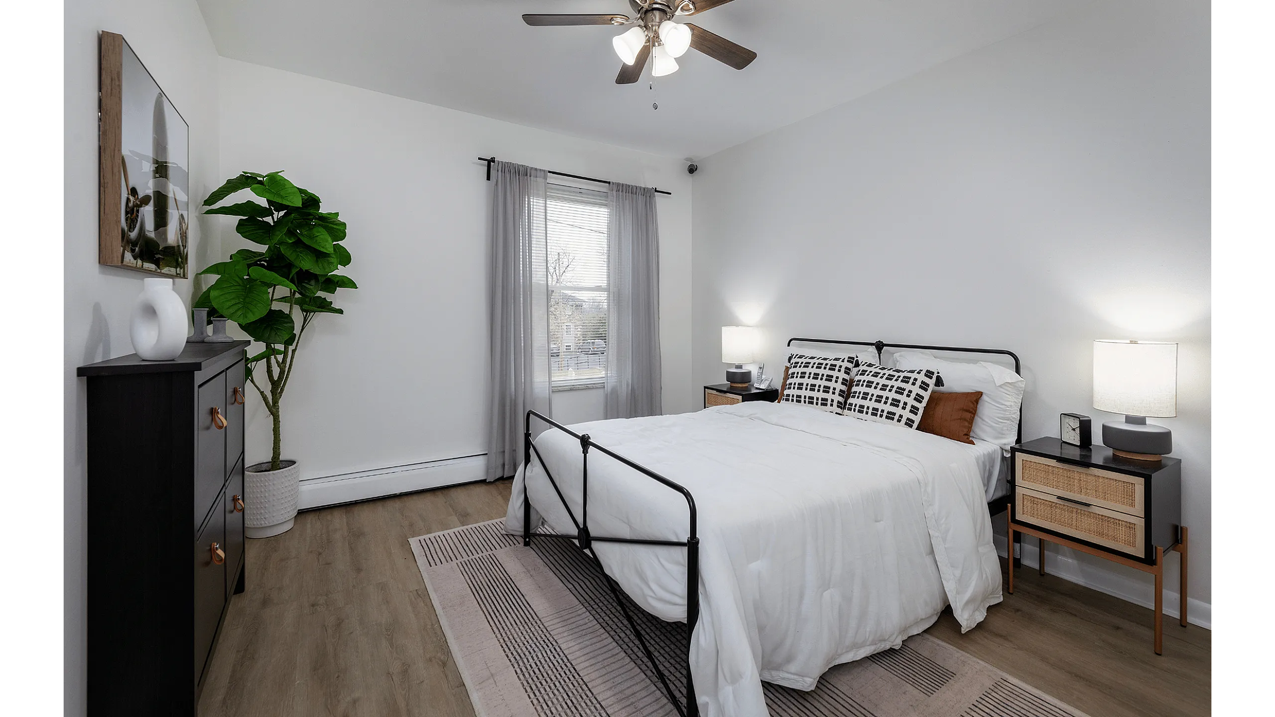 Inviting bedroom featuring a cozy bed with modern decor, a stylish dresser, and a large potted plant, offering a tranquil retreat.
