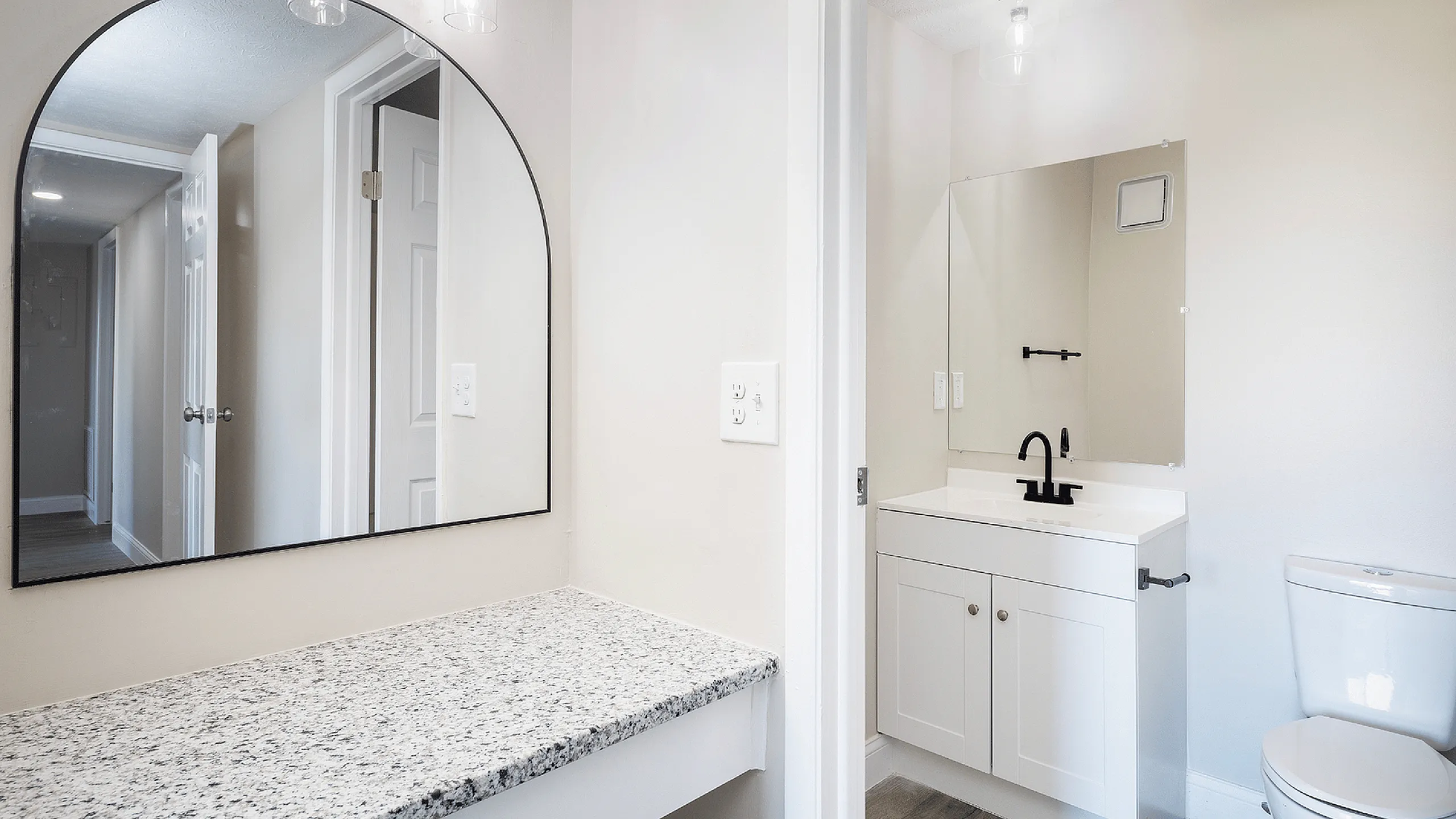 Fairfield Square Apartments Renovated Bathroom, aModern bathroom with a sleek granite countertop vanity, stylish arched mirror, and contemporary black fixtures, offering a chic and elegant design.