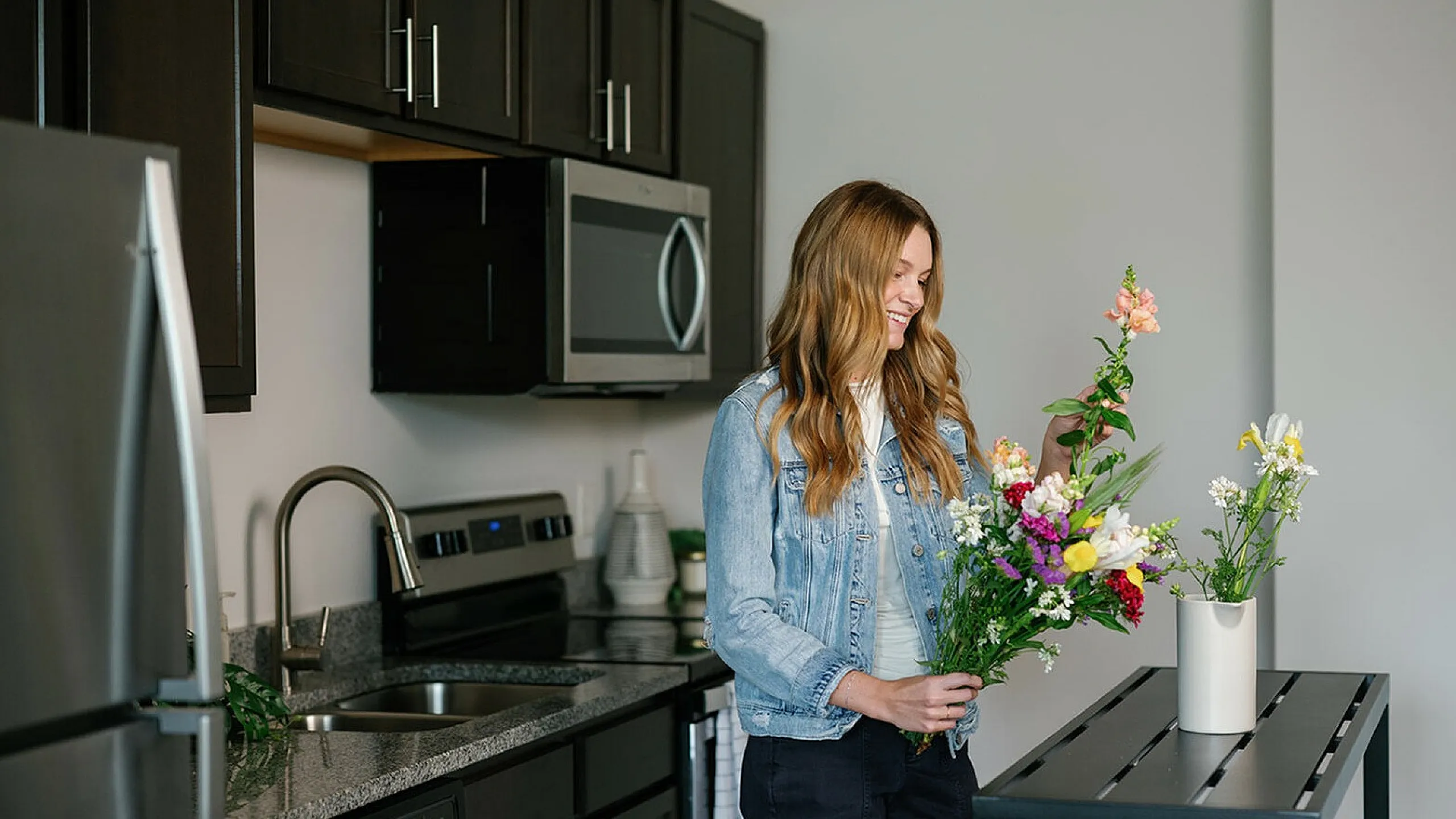 Bright modern kitchen with sleek stainless steel appliances and elegant dark cabinetry, featuring a person arranging vibrant fresh flowers for a touch of nature and warmth. The Ave apartments in Clintonville, The Ave apartments in columbus