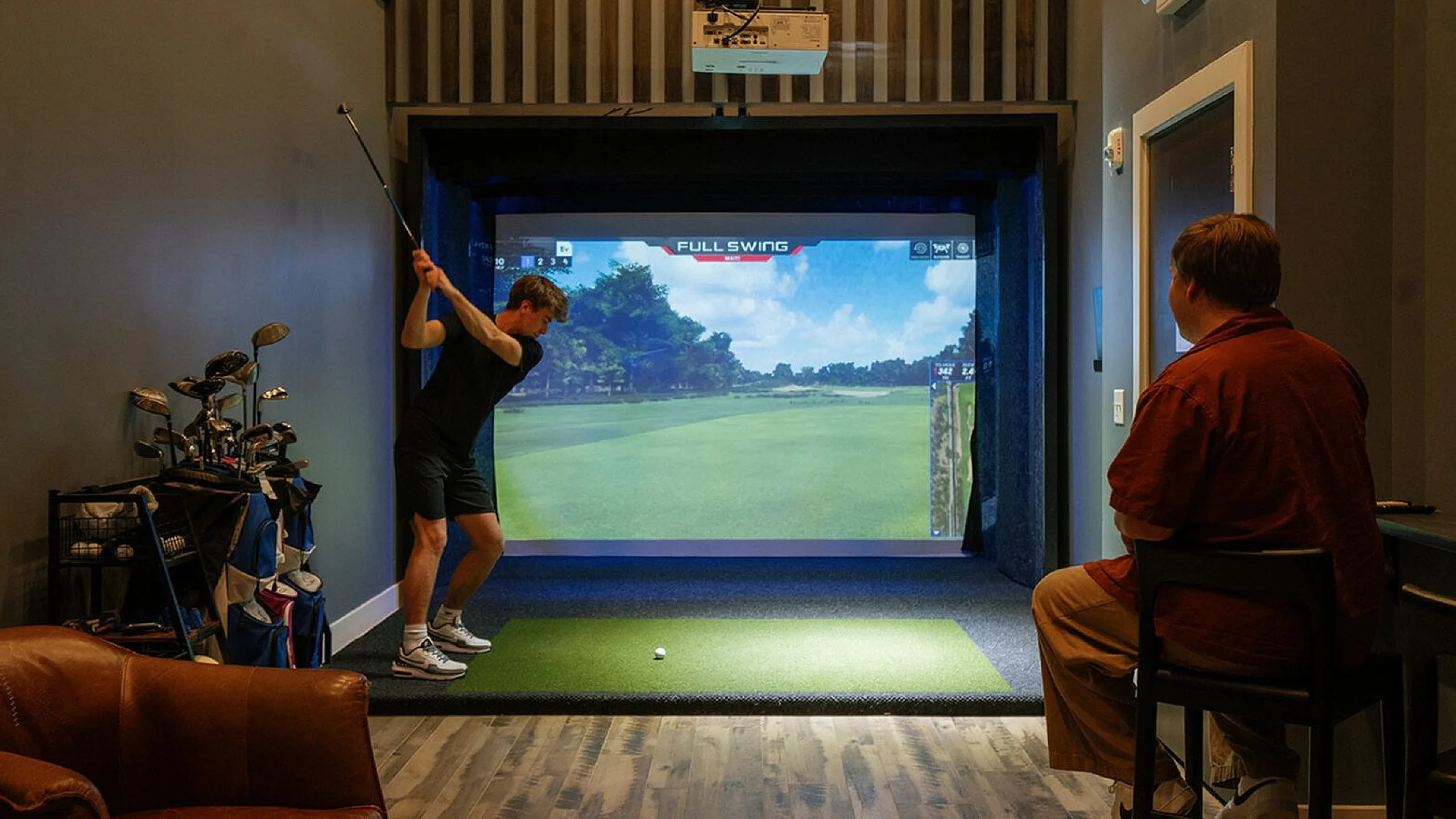 Modern indoor golf simulator room featuring a player swinging a club with realistic virtual golf course projection. The Ave apartments in Clintonville, The Ave apartments in columbus ohio, columbus ohio apartments, one bedroom apartments Co