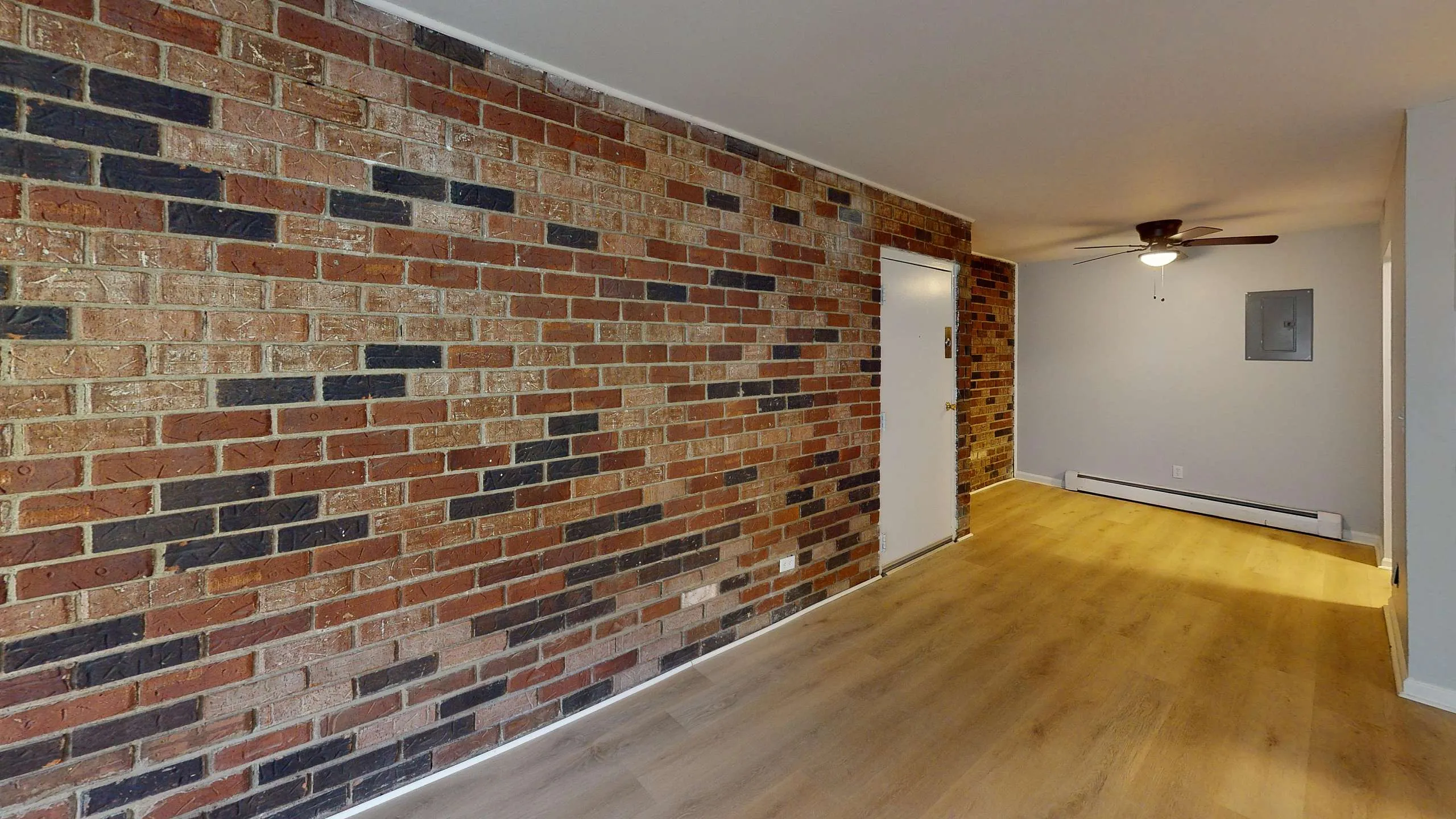 Chic apartment interior featuring a striking exposed brick wall, sleek wooden flooring, and modern ceiling fan.
