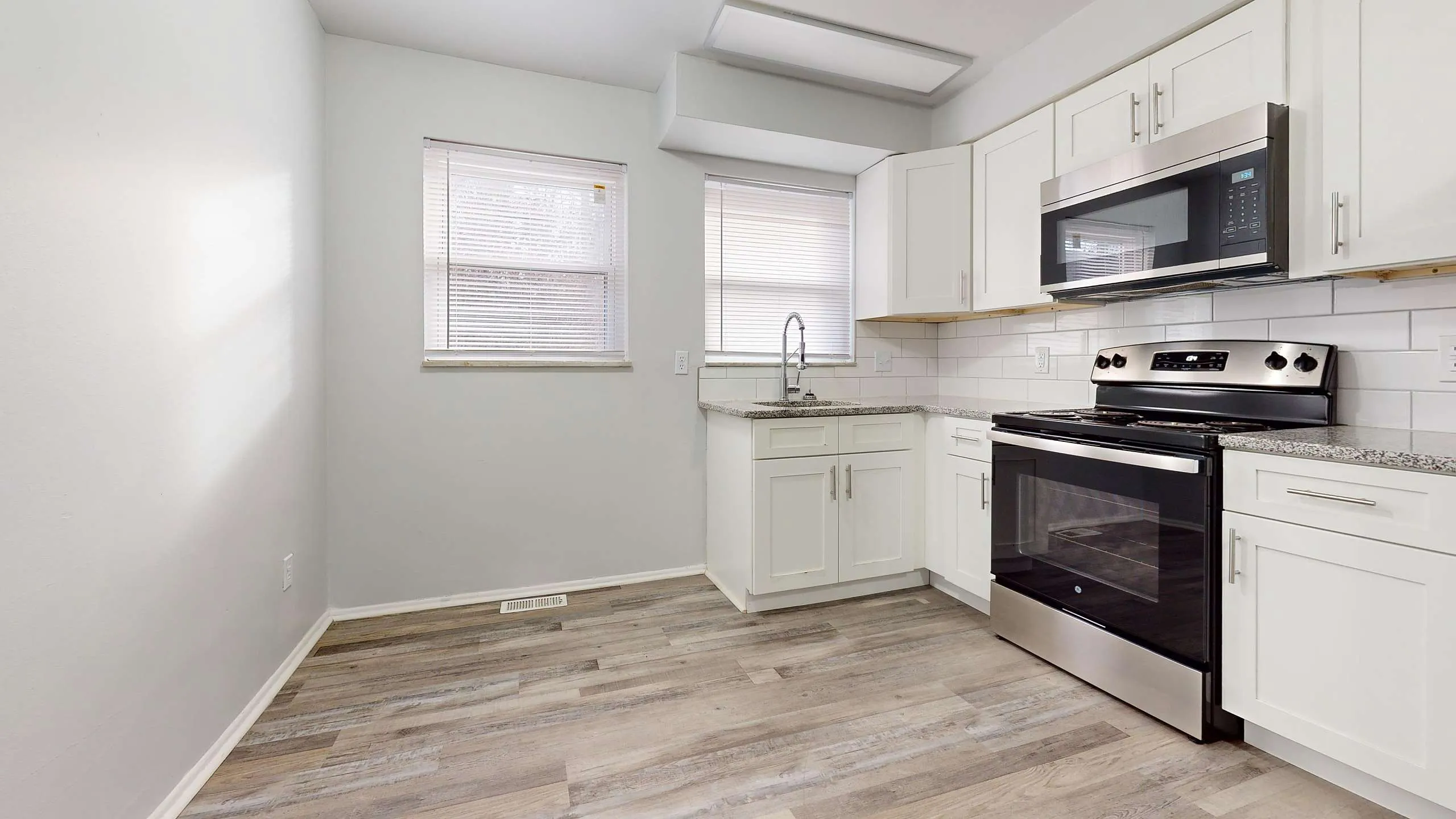 Bright and modern kitchen with sleek stainless steel appliances, elegant white cabinetry, and stylish wood flooring.
