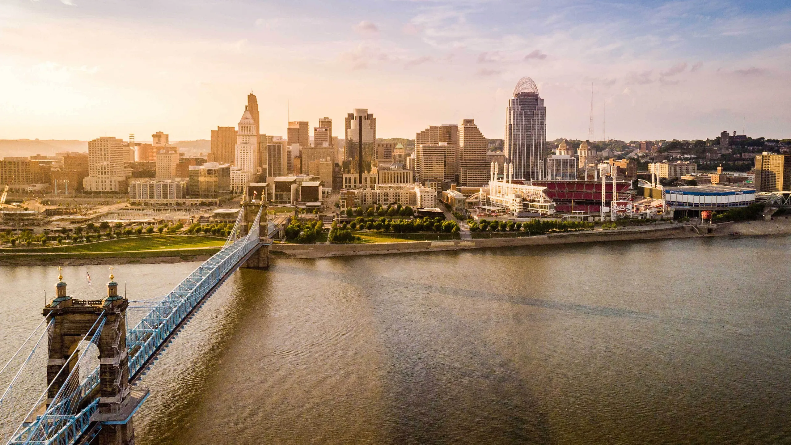 Breathtaking aerial view of a vibrant city skyline at sunset, with a historic suspension bridge gracefully spanning over a calm river.