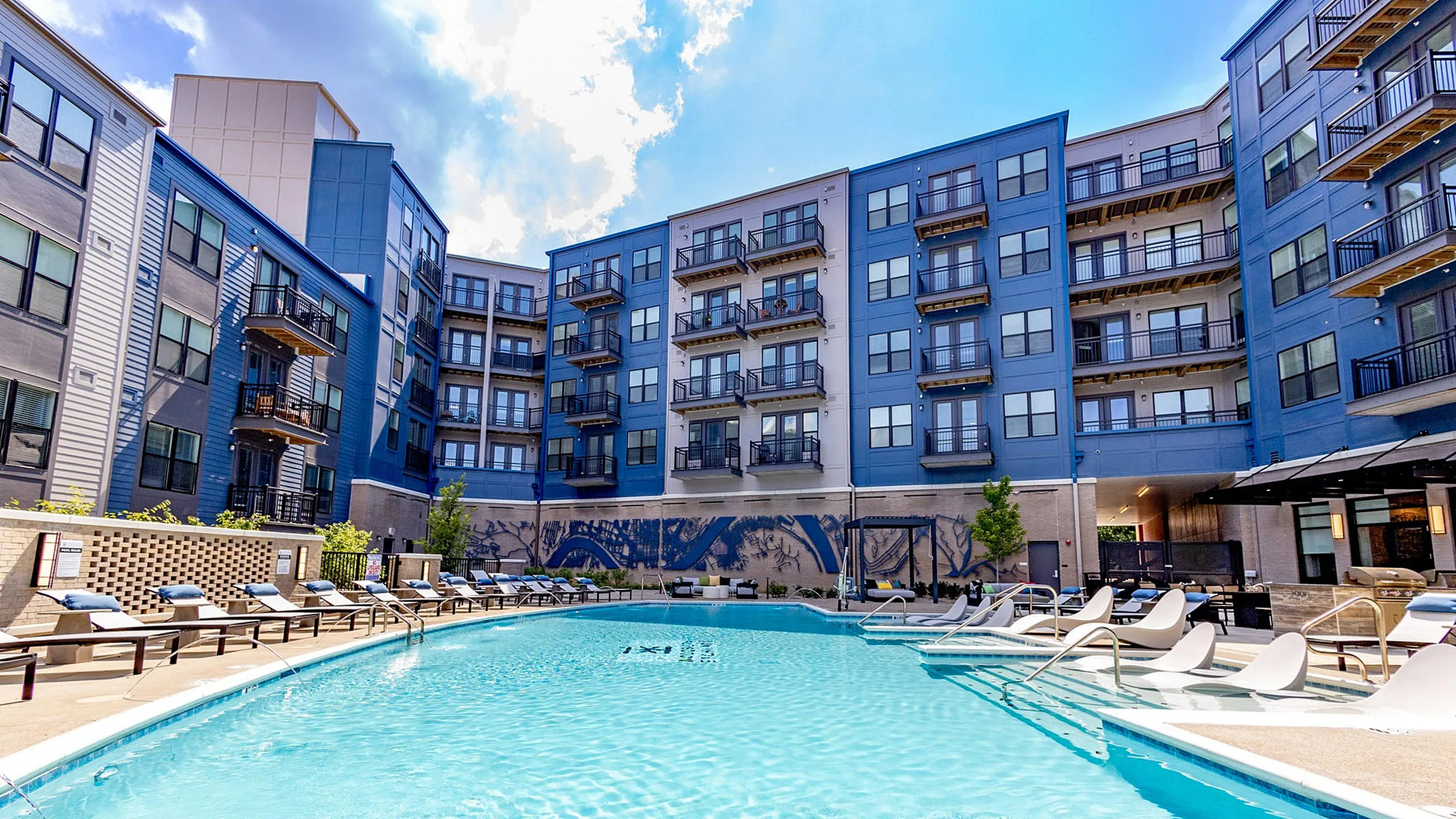 Woodburn Exchange Apartments in East Walnut Hills, Luxurious apartment complex with stunning blue exterior, featuring a sparkling pool surrounded by comfortable lounge chairs, perfect for relaxation and leisure.