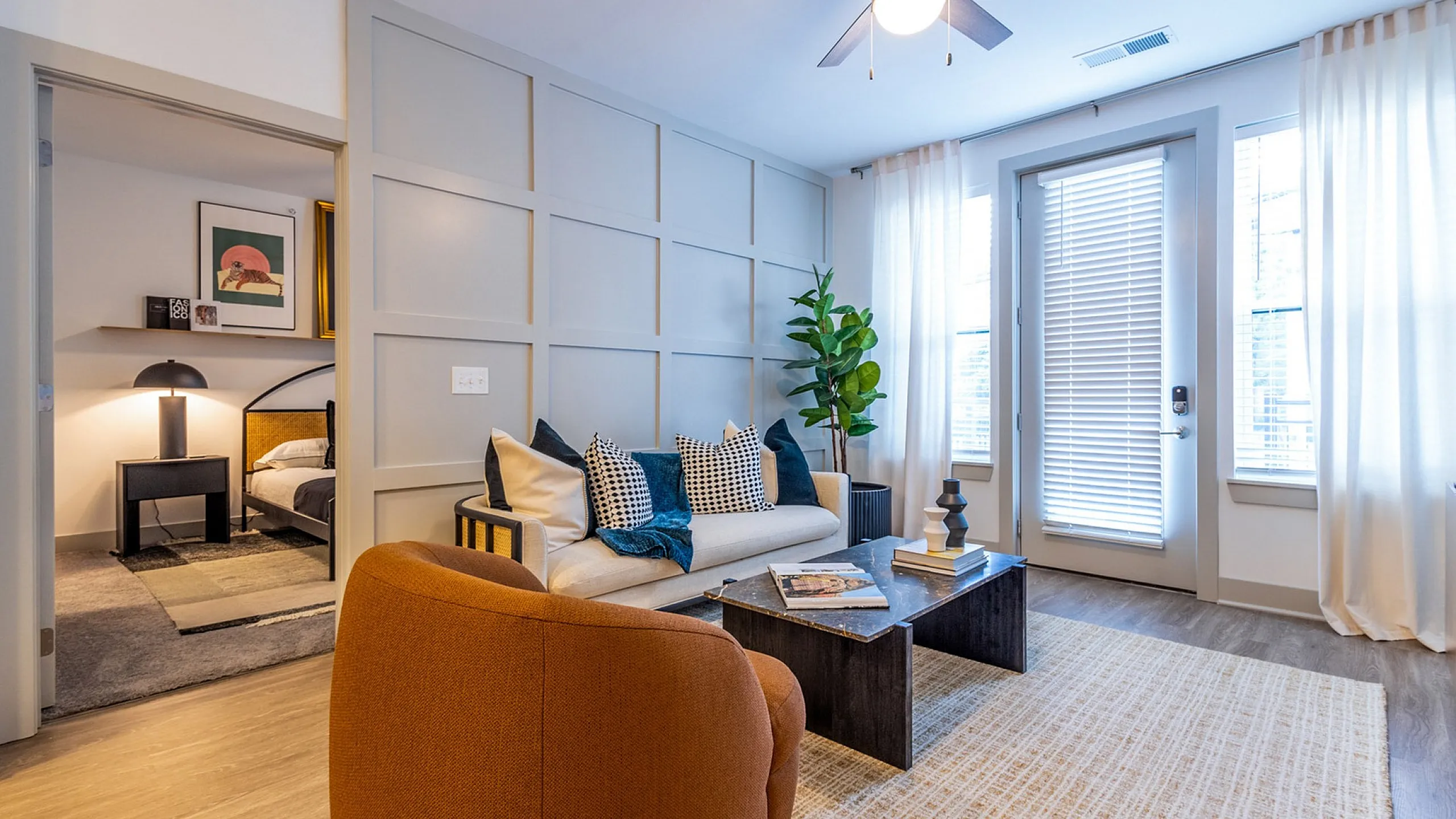 Modern living room with stylish decor, featuring a cozy sofa with accent pillows, a chic coffee table, and a bright ambiance from large windows and a ceiling fan.