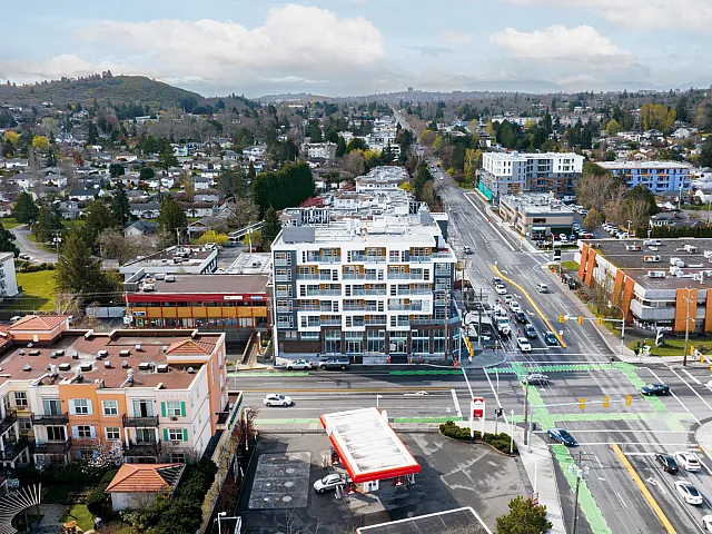Aerial view of a vibrant urban neighborhood with modern apartments, bustling streets, and scenic greenery in the background.