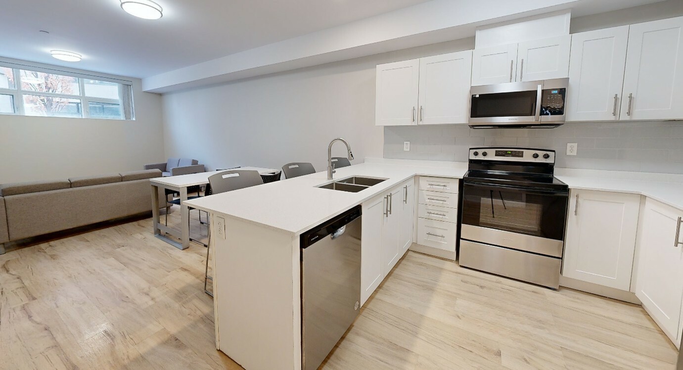 Modern open-concept kitchen and living area with sleek white cabinetry, stainless steel appliances, and bright natural lighting.