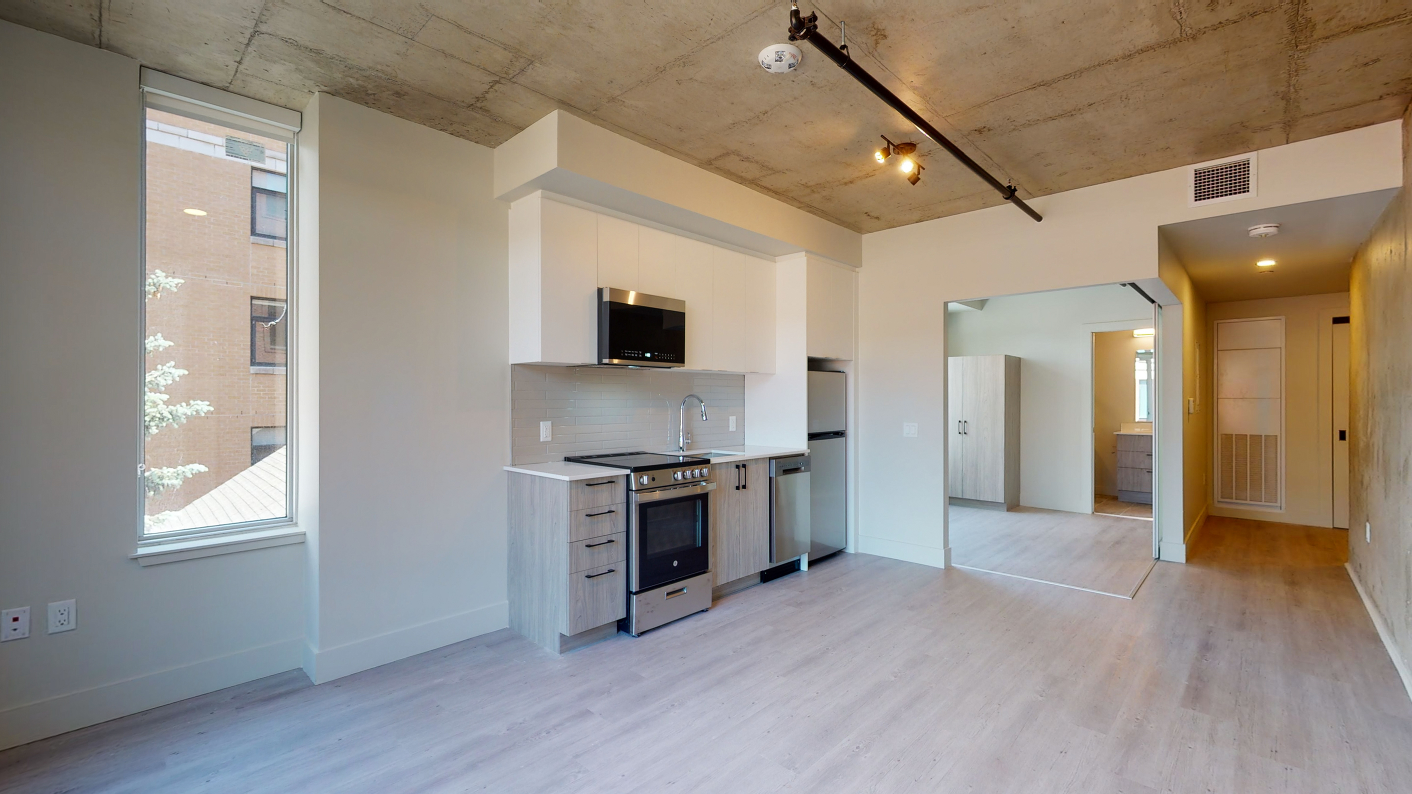 Modern apartment interior featuring an open-concept kitchen with sleek appliances, large windows offering natural light, and a concrete ceiling for an industrial touch.