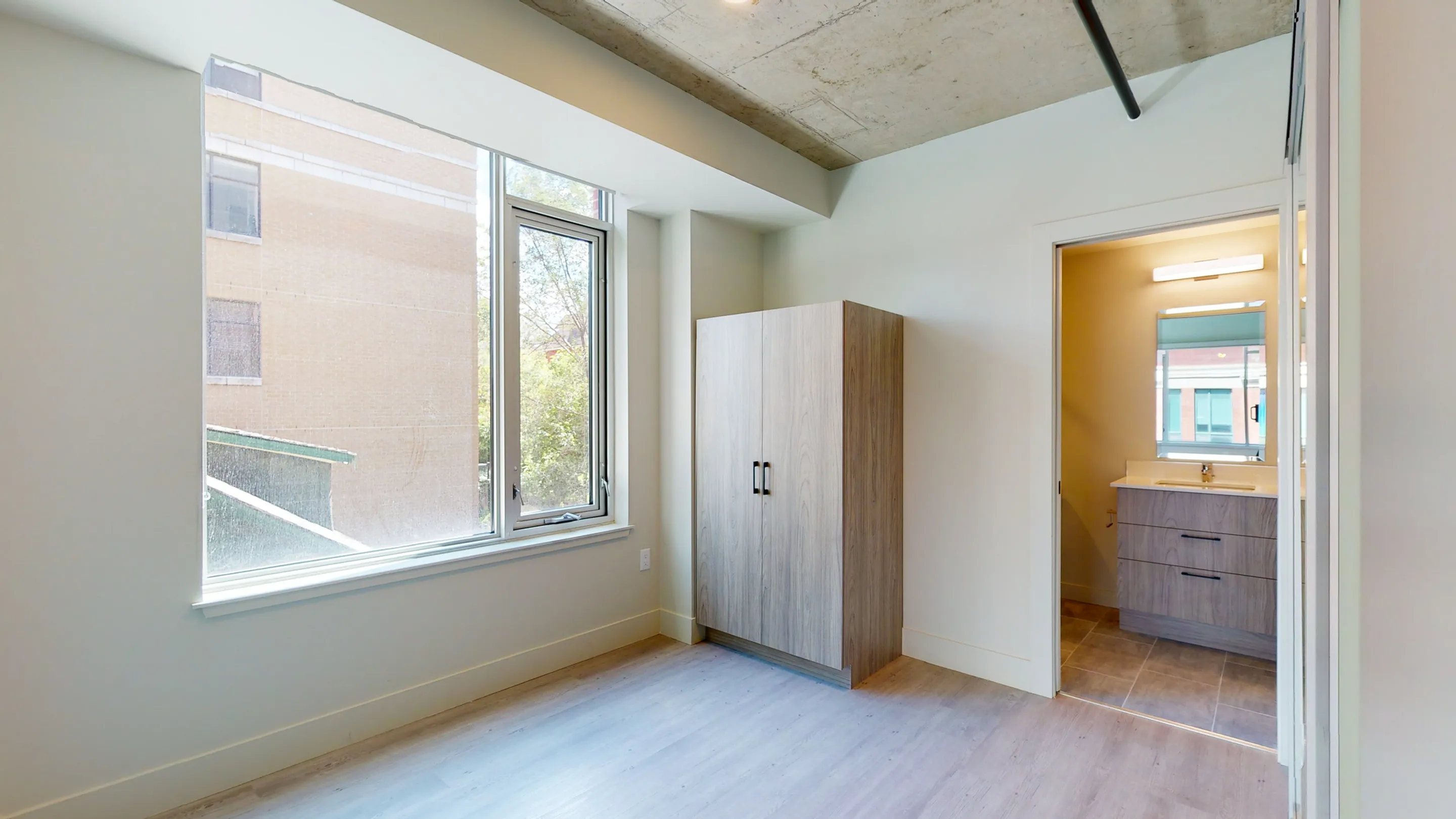 Bright, minimalist bedroom with large window and modern wardrobe, adjacent to sleek bathroom.