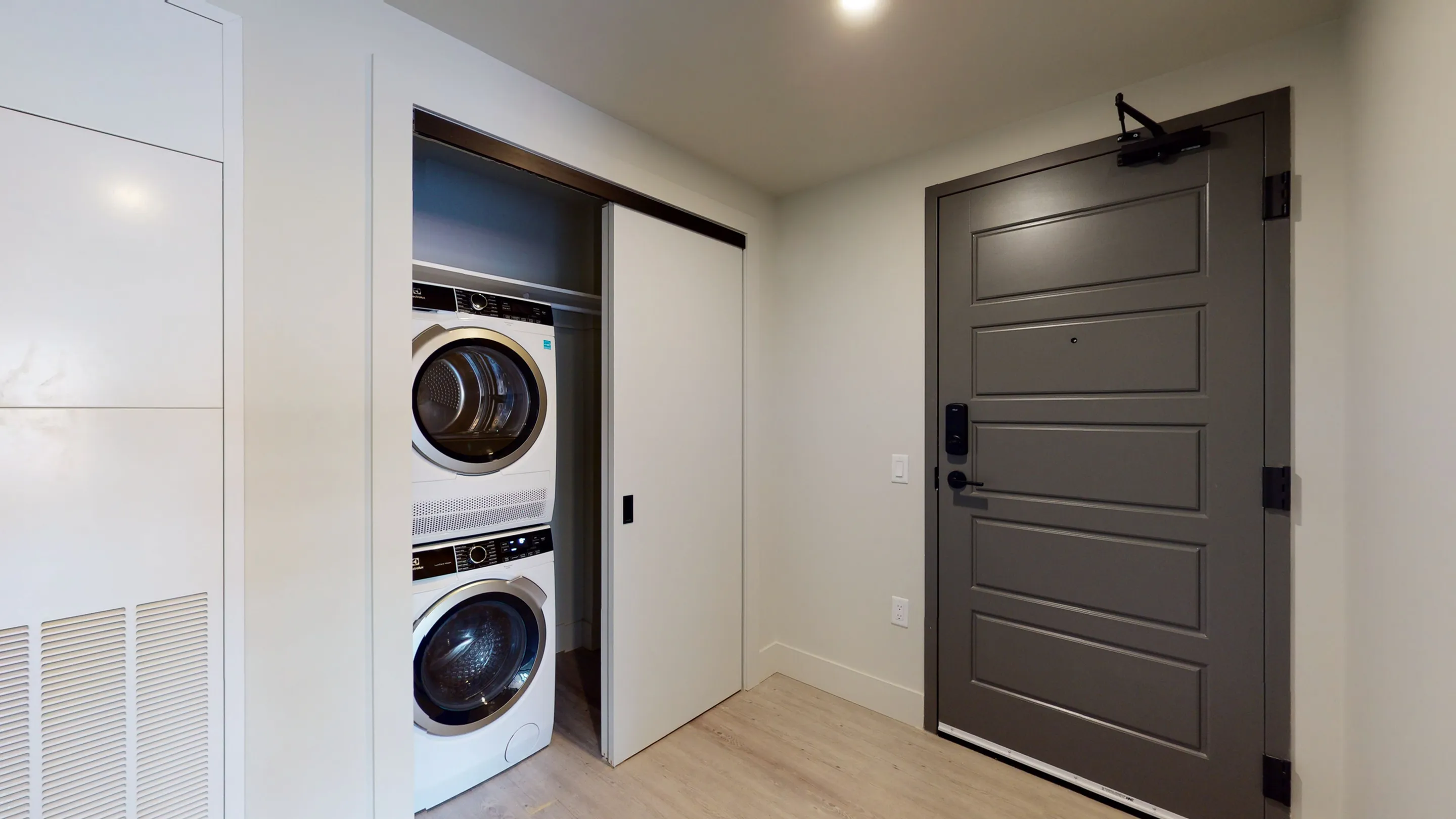 Sleek apartment entryway featuring a modern front door and a compact laundry nook with stacked washer and dryer.