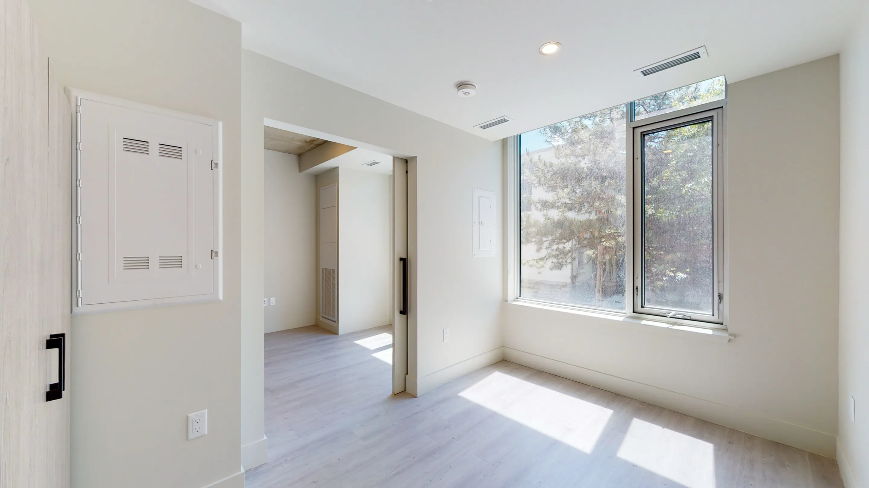 Bright, airy apartment room featuring large windows, minimalist decor, and sleek hardwood floors, perfect for modern living.