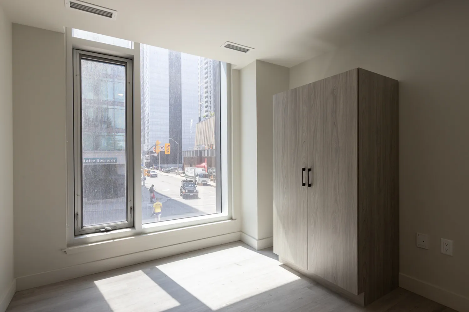 Bright urban apartment bedroom with large window offering cityscape views and a modern wardrobe.