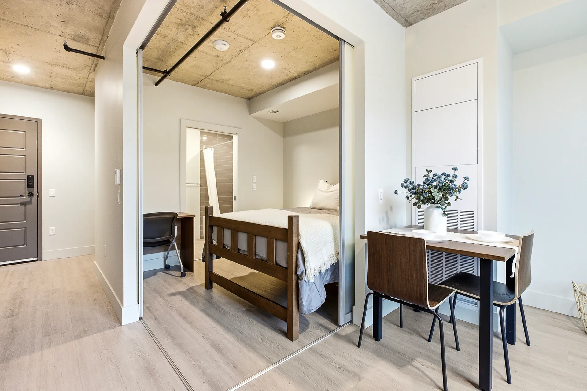 Modern studio apartment featuring a cozy bedroom with sliding doors, a compact dining area with elegant decor, and a stylish workspace.