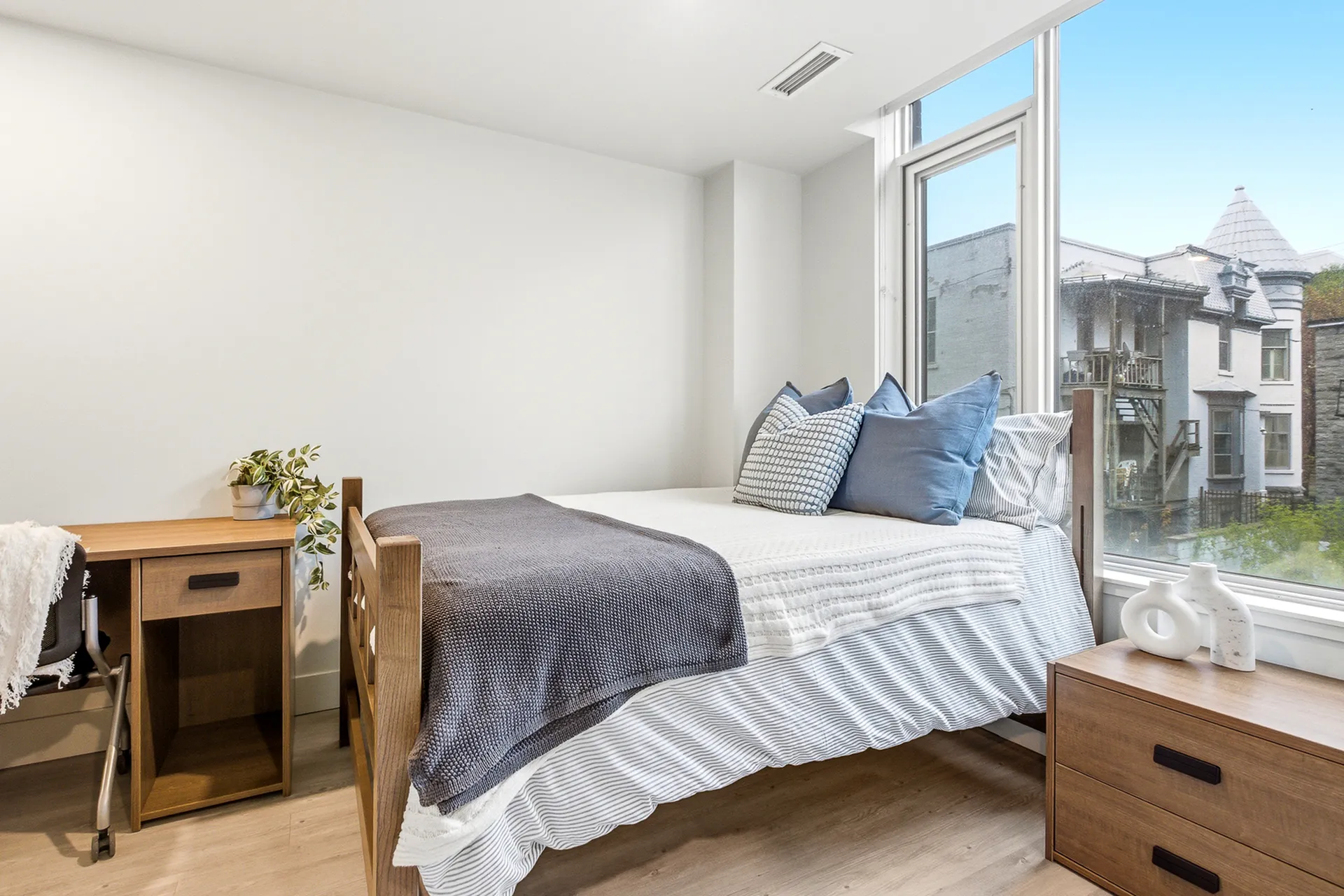 Bright and cozy bedroom featuring a stylish bed with plush pillows, modern wooden furniture, and a large window with scenic views.