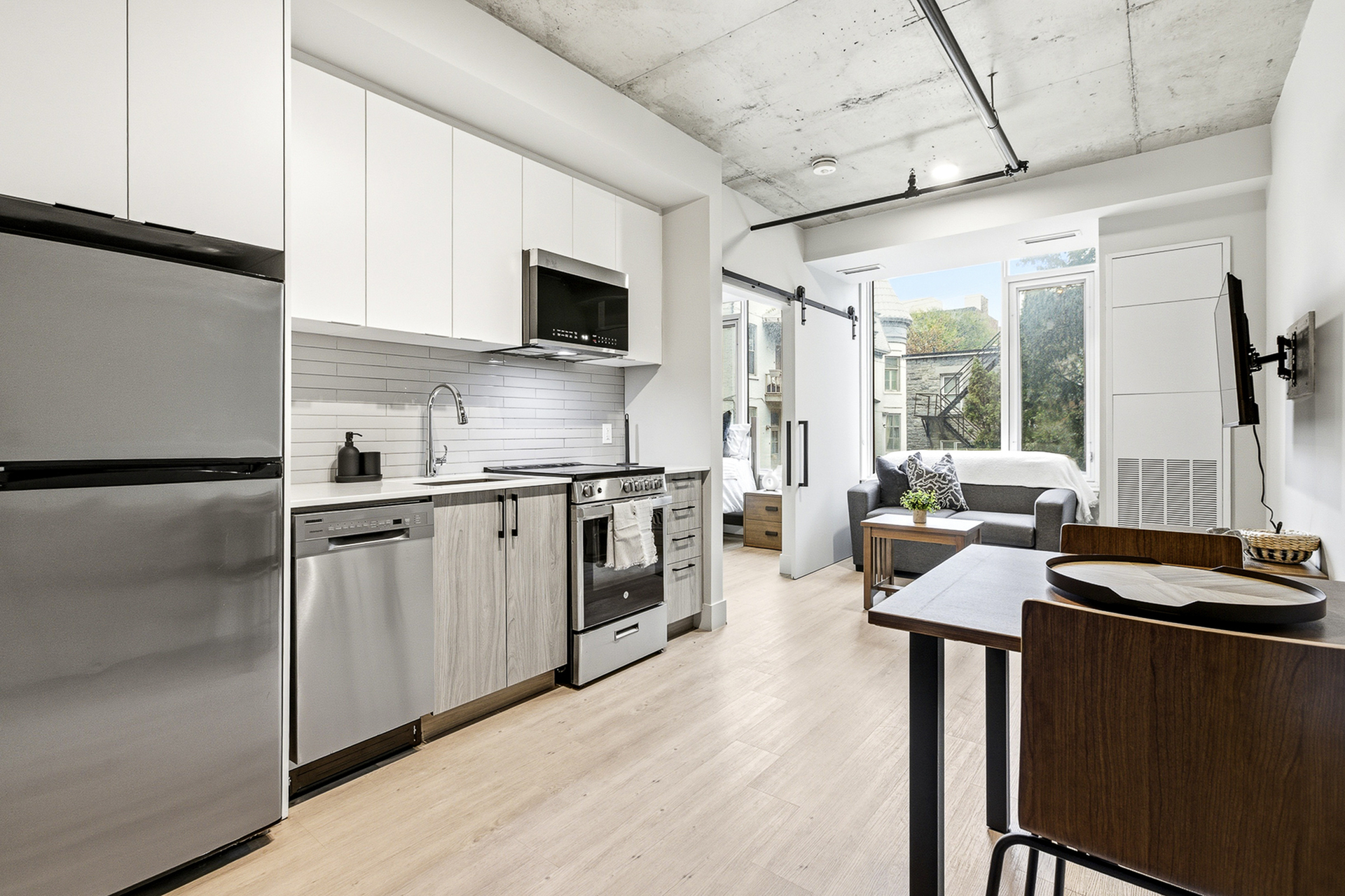 Contemporary apartment interior featuring a sleek kitchen with stainless steel appliances, an open living area with modern furniture, and large windows inviting natural light.