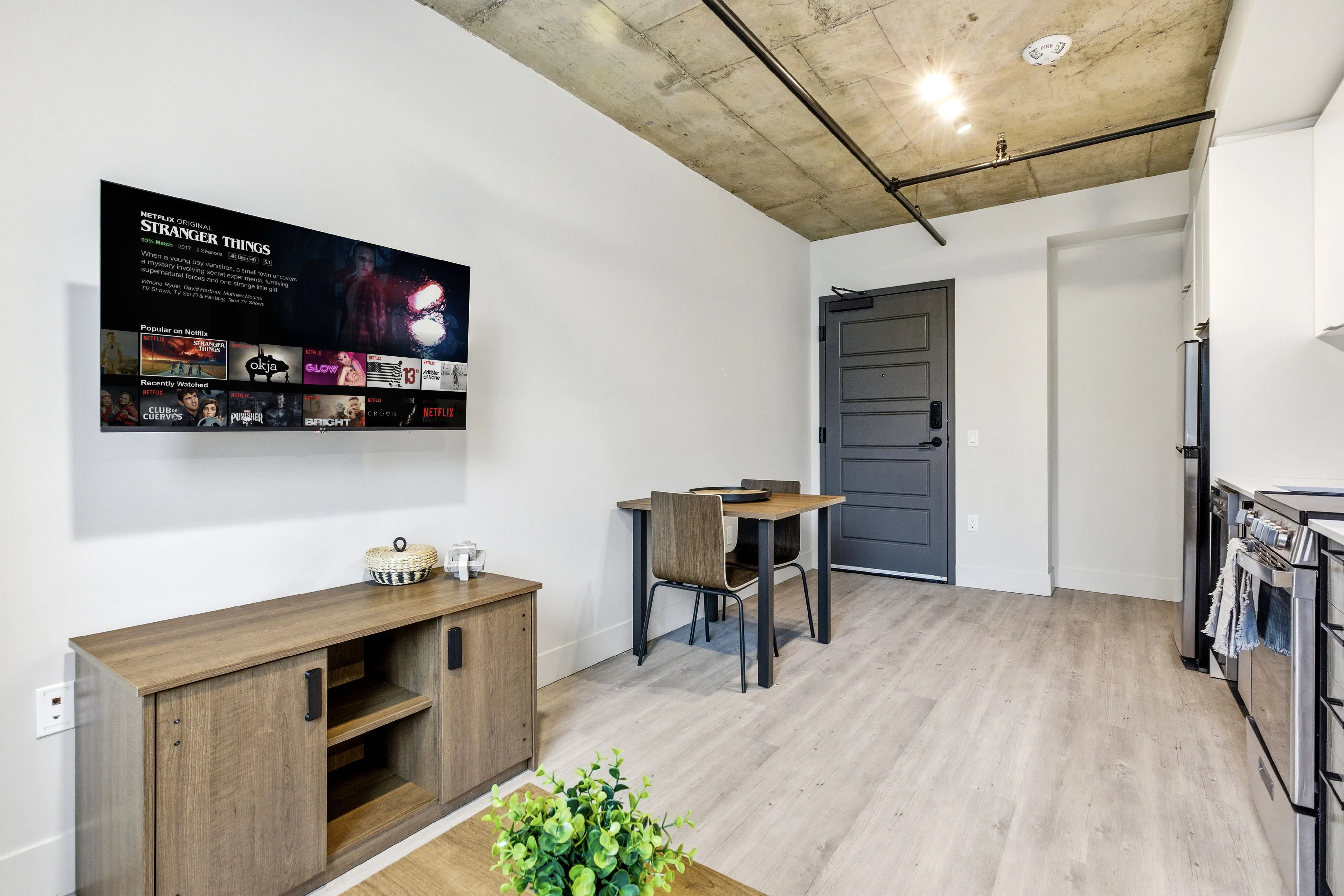 Modern living area featuring sleek furnishings, a wall-mounted TV, and a dining nook in an open-concept apartment.
