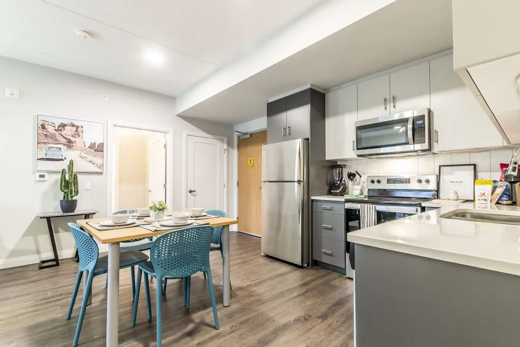 Modern kitchen and dining area with sleek appliances, elegant cabinetry, and vibrant blue chairs creating a welcoming space.