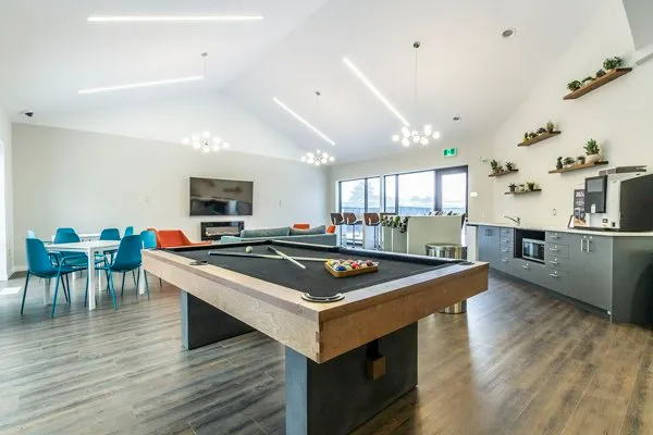 Modern communal living space featuring a sleek pool table, dining area, and contemporary kitchen with stylish lighting and floor-to-ceiling windows.