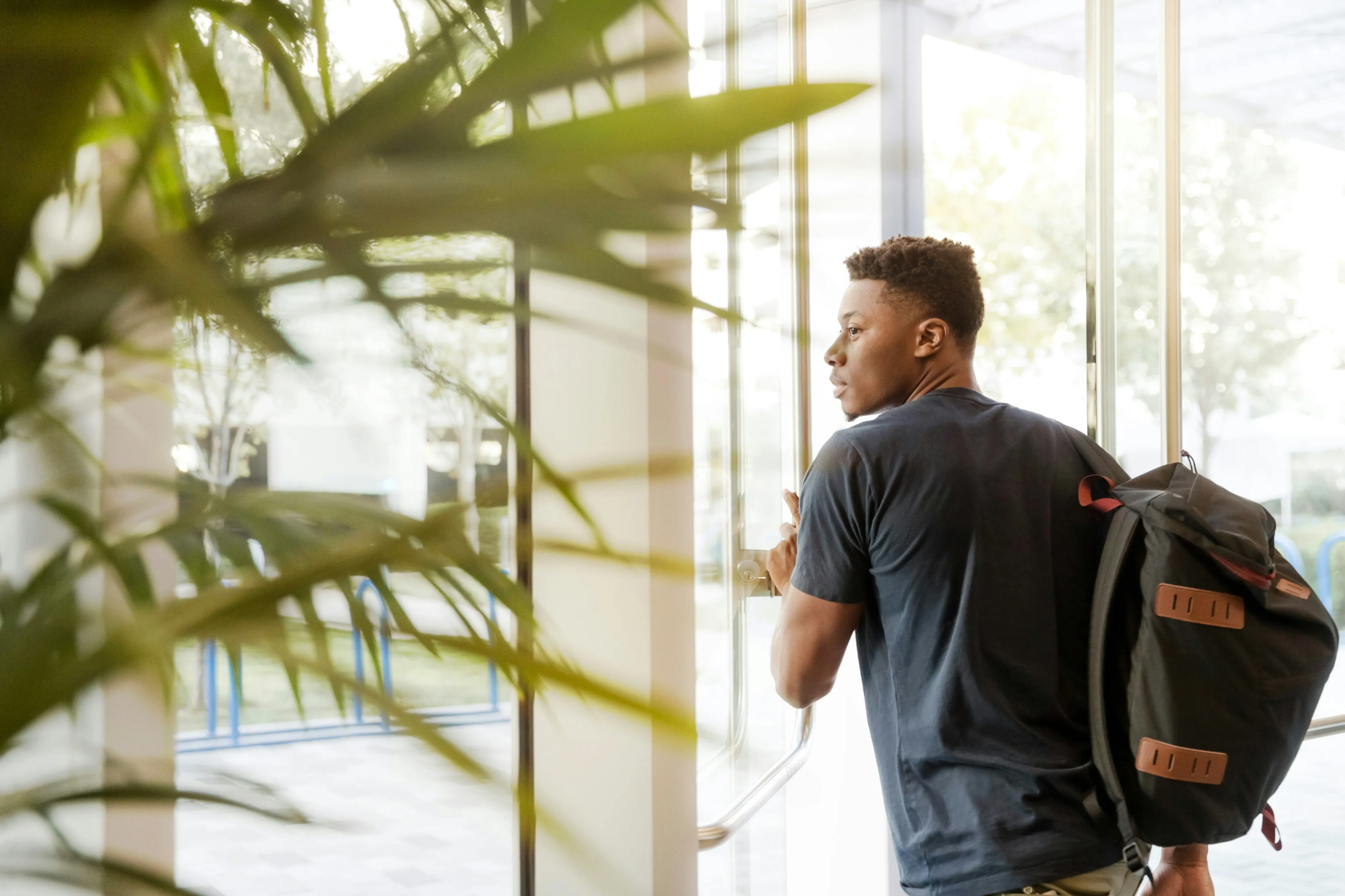 Bright and modern entrance with lush greenery, showcasing a welcoming atmosphere as a person with a backpack enters the building.